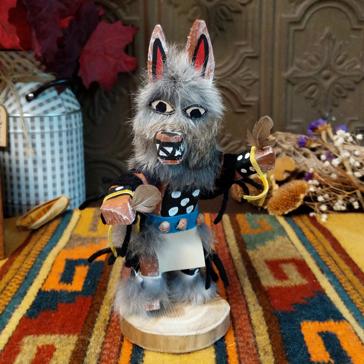 Navajo Wolf Kachina doll with gray fur, pointed ears, painted teeth, black clothing with white spots, and feather accents.