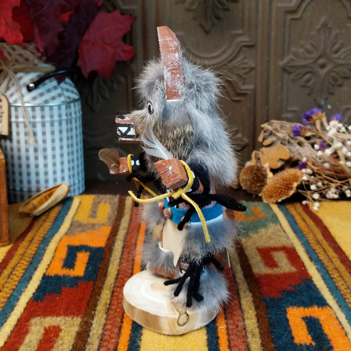 Side view of the Navajo Wolf Kachina doll with gray fur, pointed ears, painted teeth, black clothing with white spots, and feather accents.