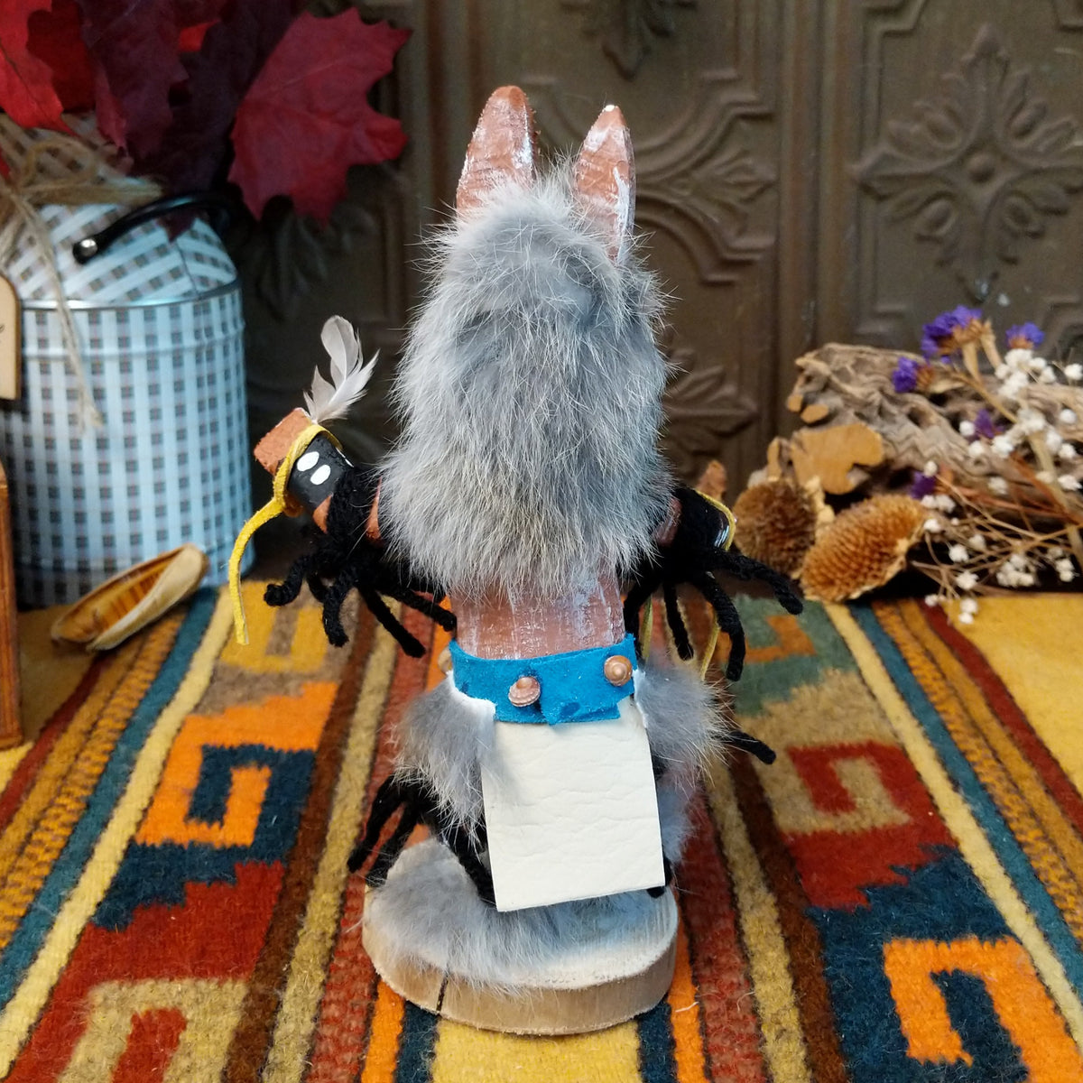 Back view of the Navajo Wolf Kachina doll with gray fur, pointed ears, painted teeth, black clothing with white spots, and feather accents.