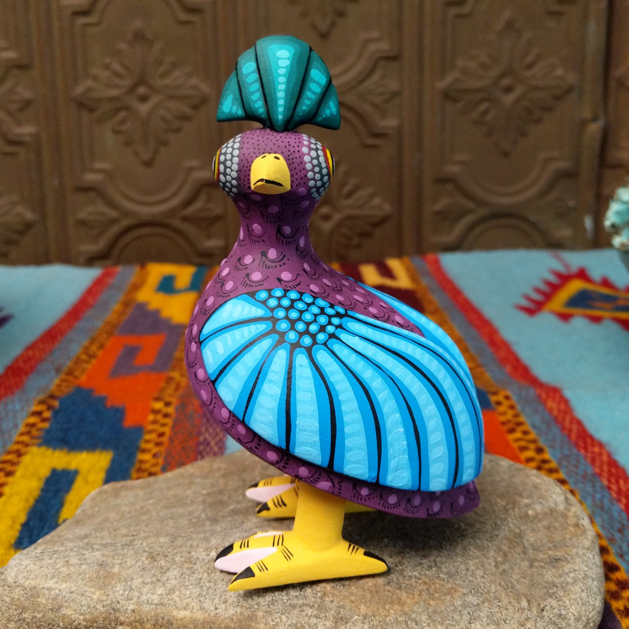 Oaxacan bird wood carving by Hedilberto Olivera with a purple body, broad blue wings, fan-shaped crest, and yellow beak and feet.