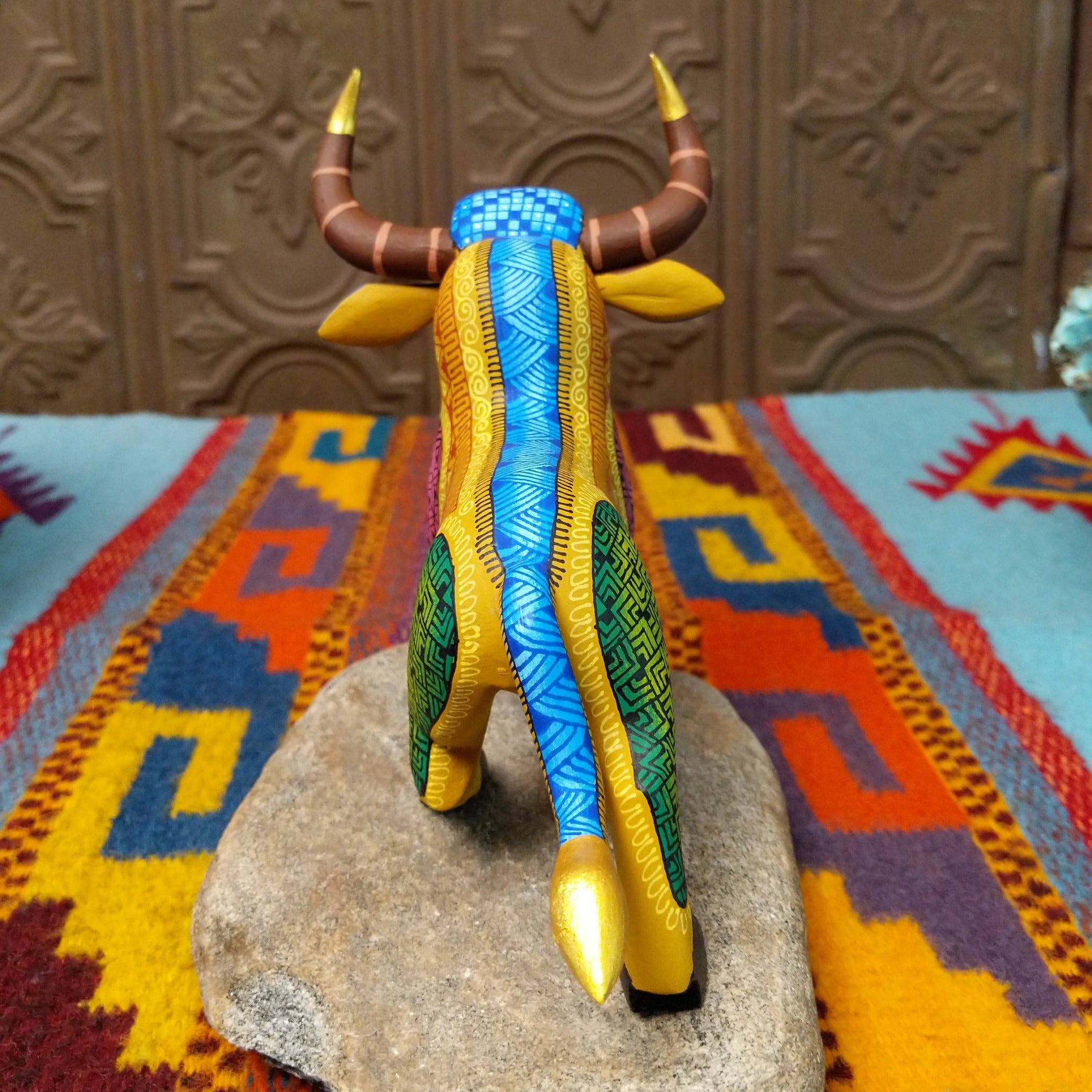 Oaxacan bull wood carving by Abundio Muñoz with curved horns, a golden yellow body, and colorful geometric patterns across the legs and torso.
