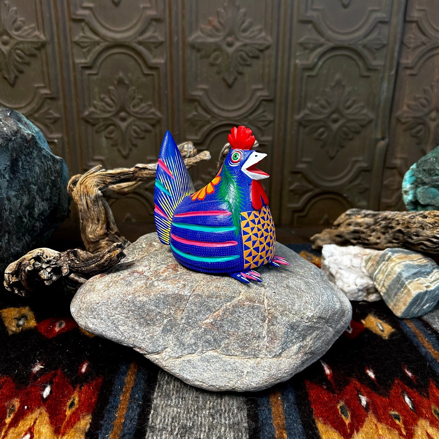 Blue chicken figurine with a red comb and wattle, featuring a yellow beak and intricate yellow eye details.