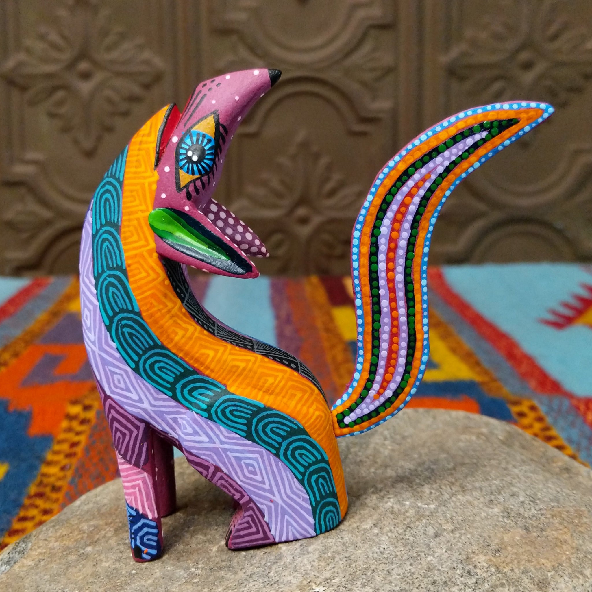 Oaxacan coyote wood carving by Julia Calvo Olivera with an arched body, raised muzzle, curled patterned tail, and colorful geometric designs.