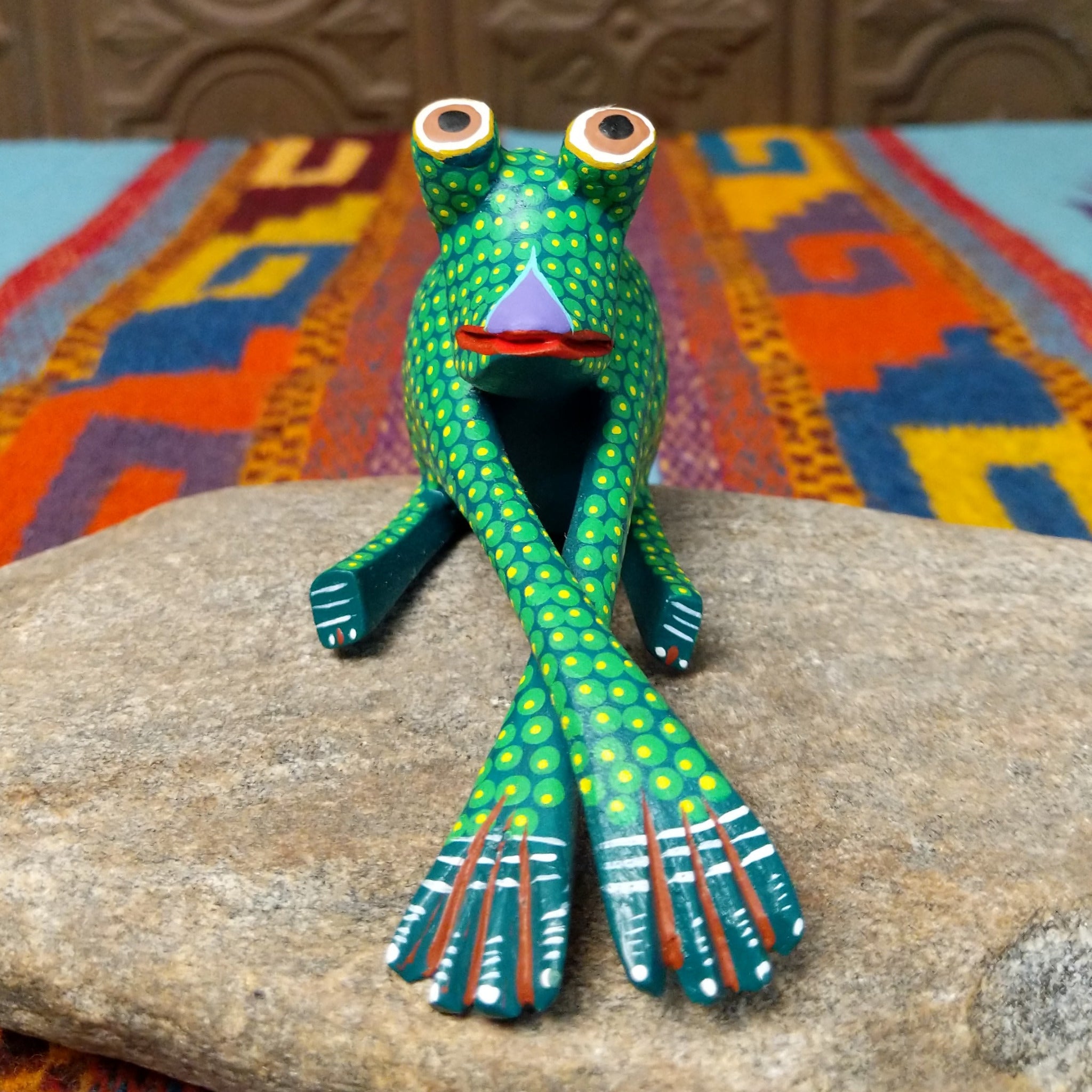 This green Oaxacan frog wood carving by Roberta Angeles features raised eyes, colorful dotted patterns, a red mouth, and long legs with oversized hand-painted webbed feet.