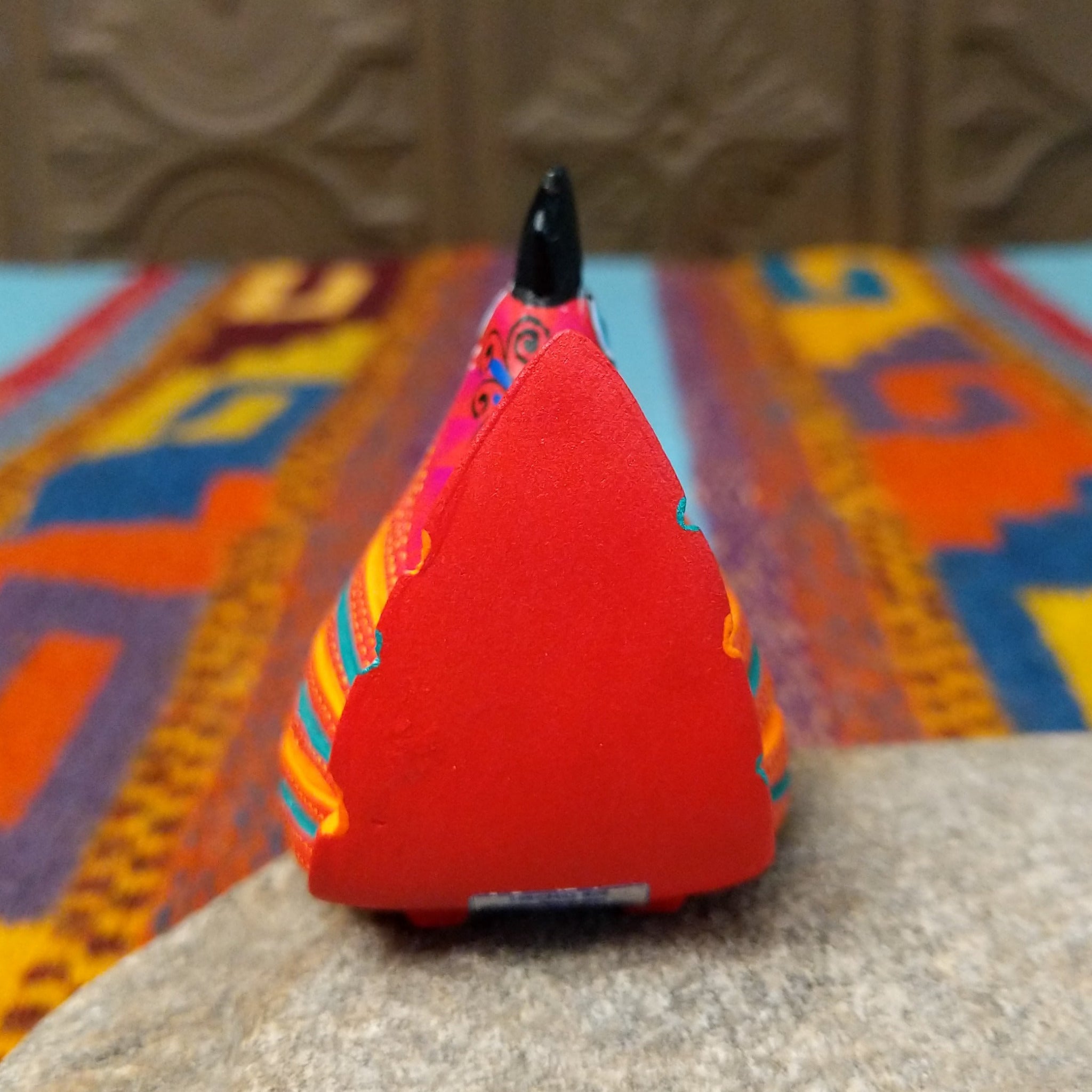 This colorful Oaxacan hen wood carving features a bright red body, black comb, turquoise eye, and intricate yellow, orange, turquoise, and black hand-painted feather patterns; rear view.