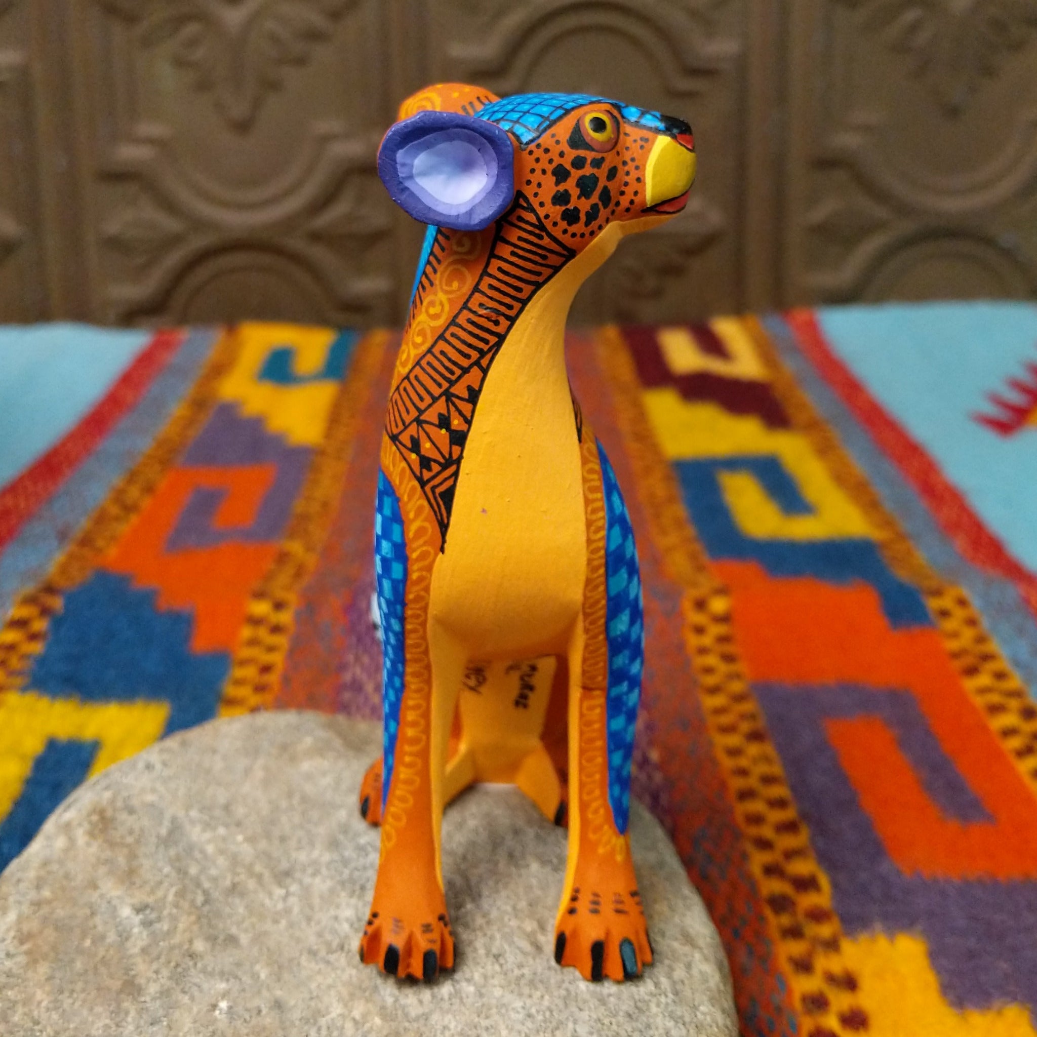 Oaxacan jaguar wood carving by Abundio Muñoz with an orange patterned body, blue legs, curled tail, and geometric painted details.