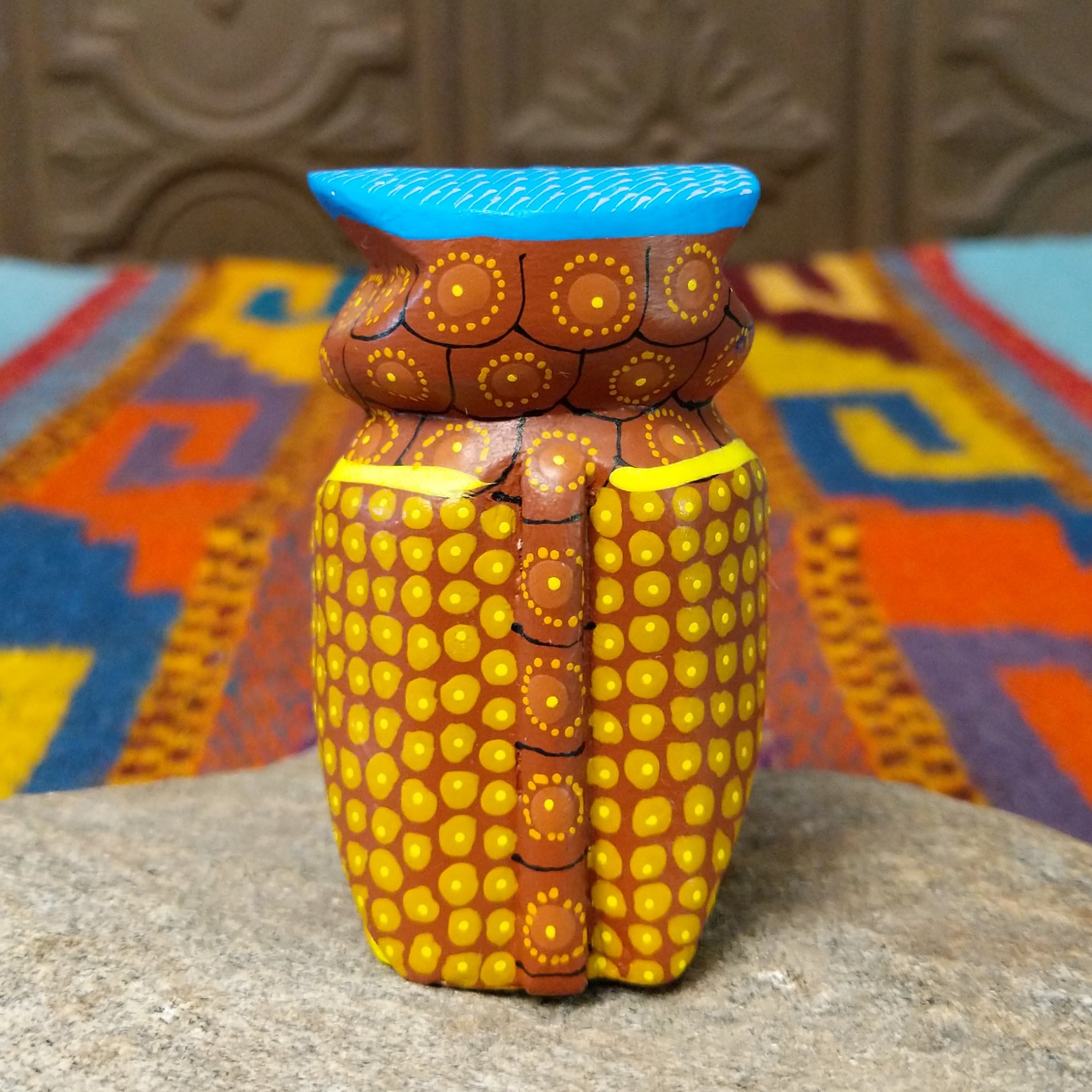 Oaxacan owl wood carving with a rounded body, large circular eyes, painted feather patterns, and a broad blue brow.