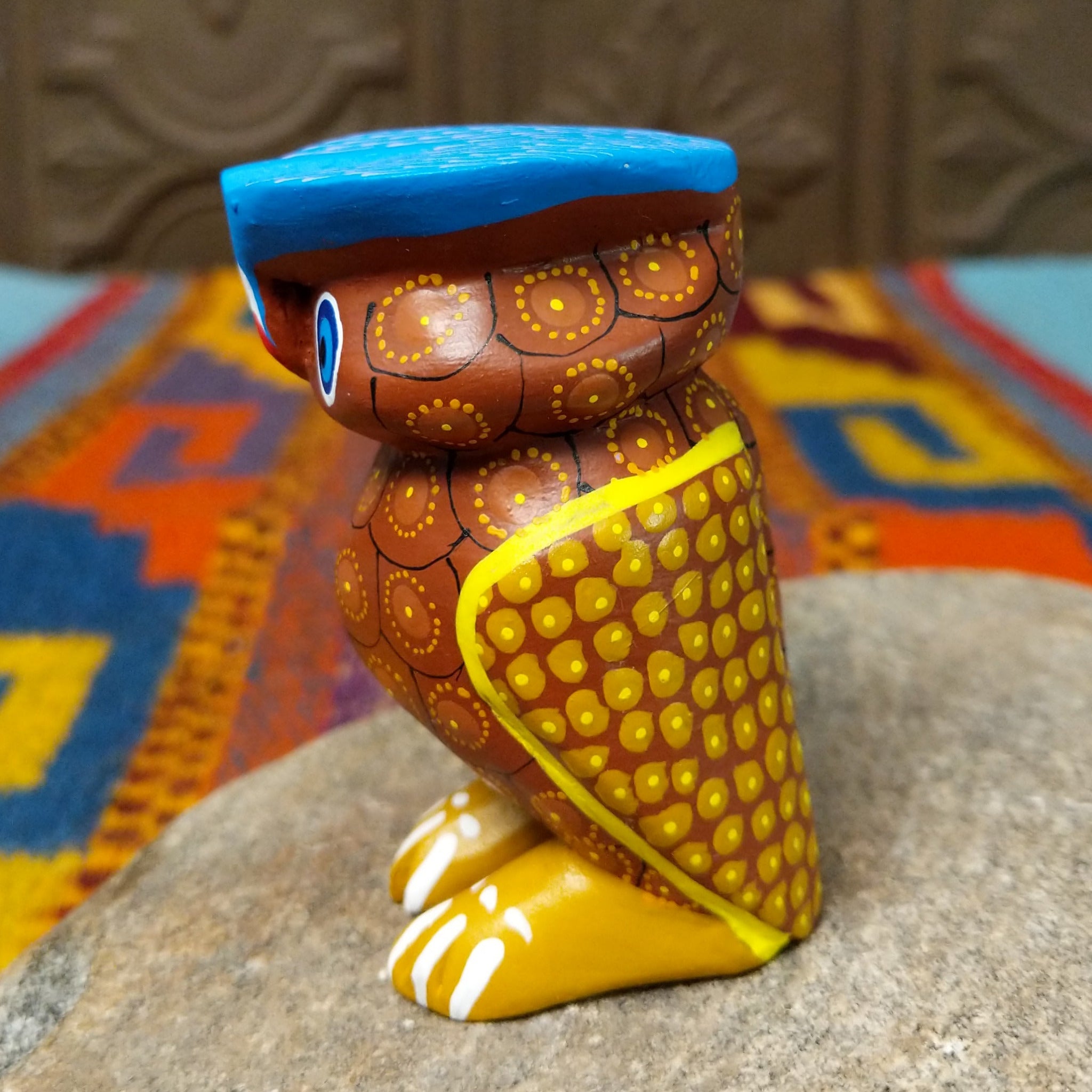 Oaxacan owl wood carving with a rounded body, large circular eyes, painted feather patterns, and a broad blue brow.