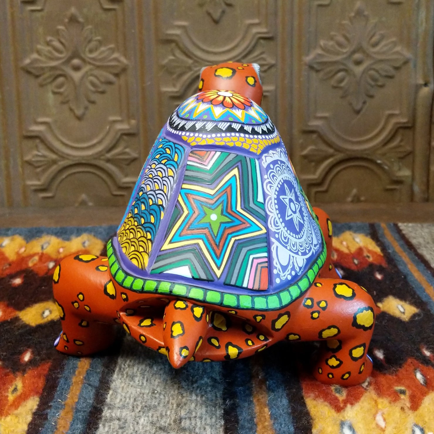 Wooden tortoise with a consistent orange base, accented by various patterns on its shell and body.