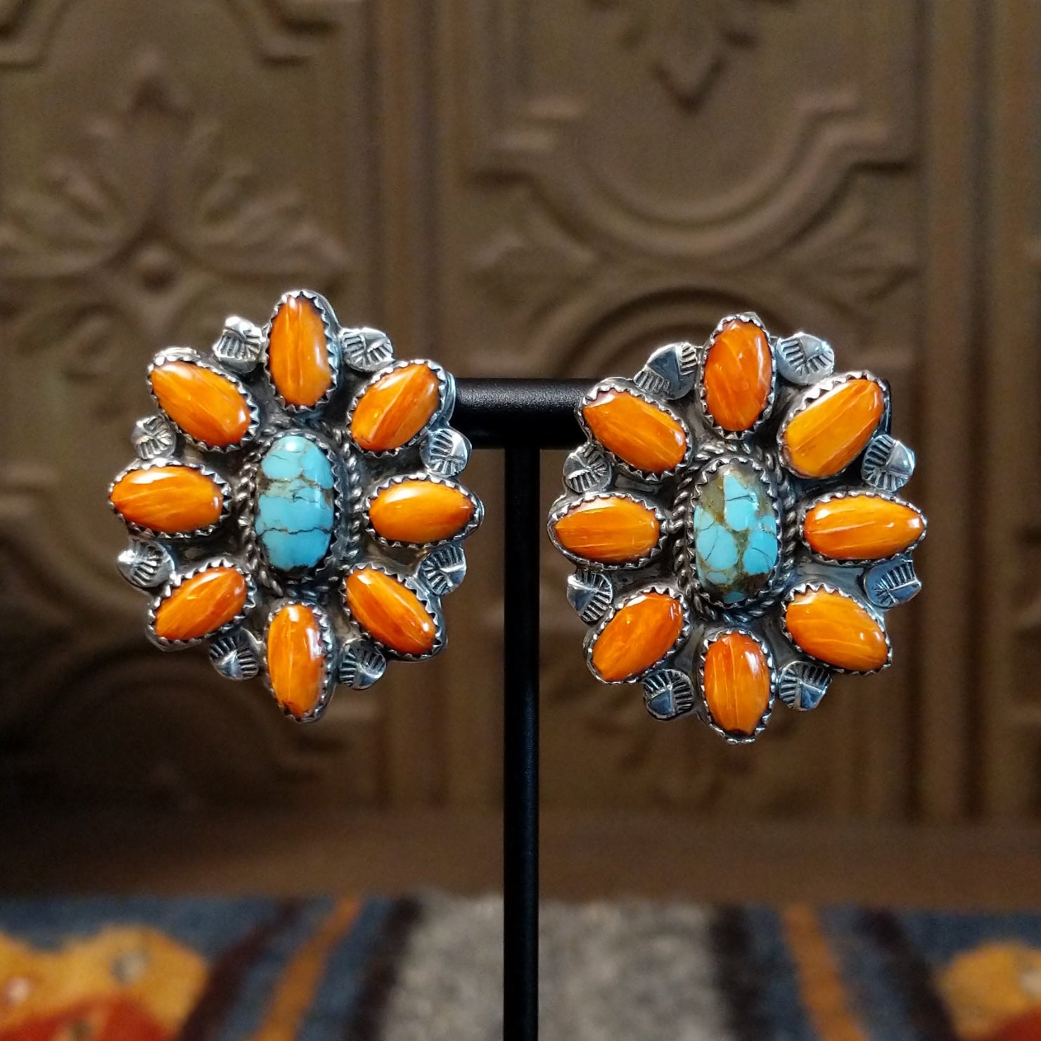 The earrings feature a cluster of orange spiny oyster shell pieces around a turquoise stone in a bezel with twisted silver rope.