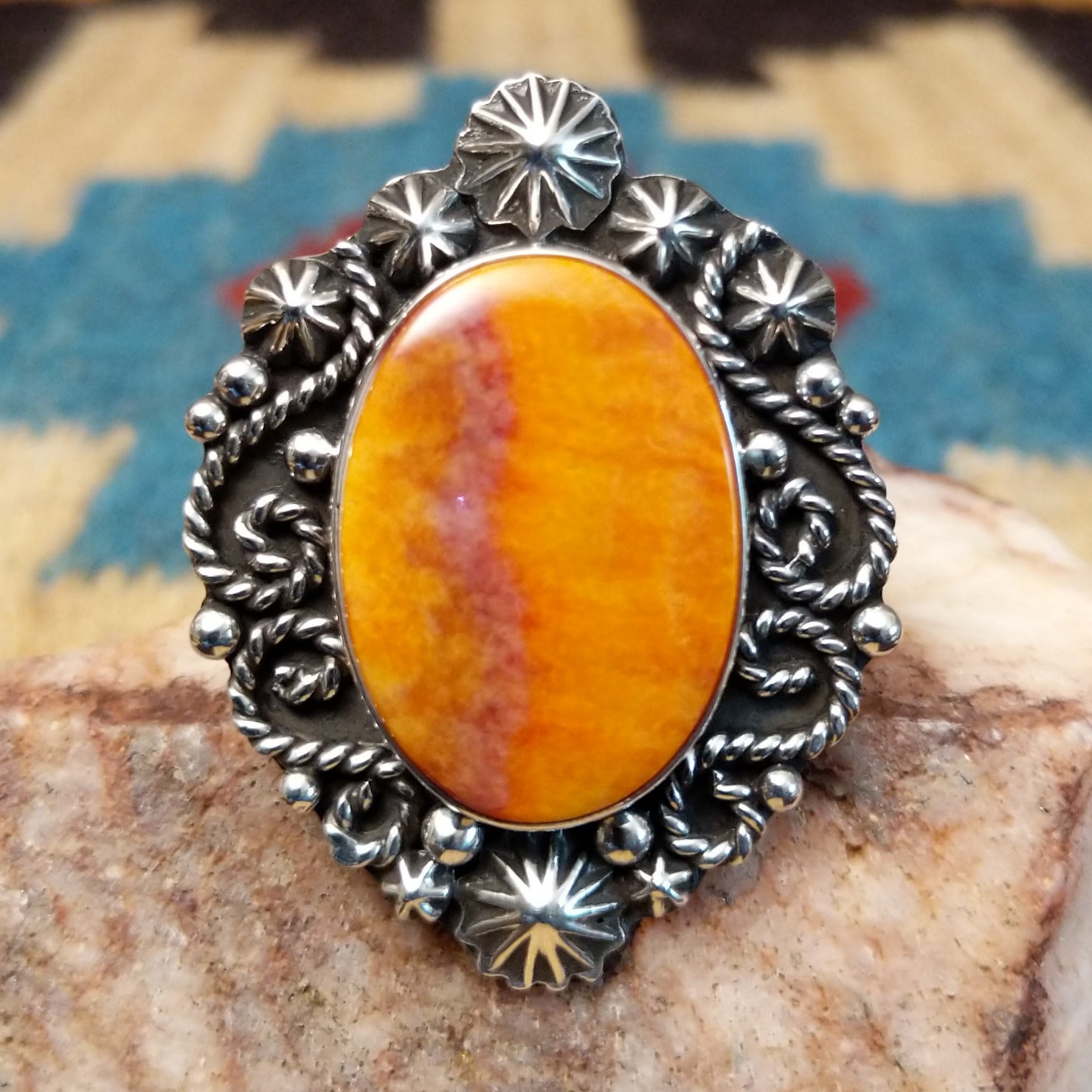 Sterling silver ring with orange spiny oyster shell set in the bezel, framed by ornate silverwork.