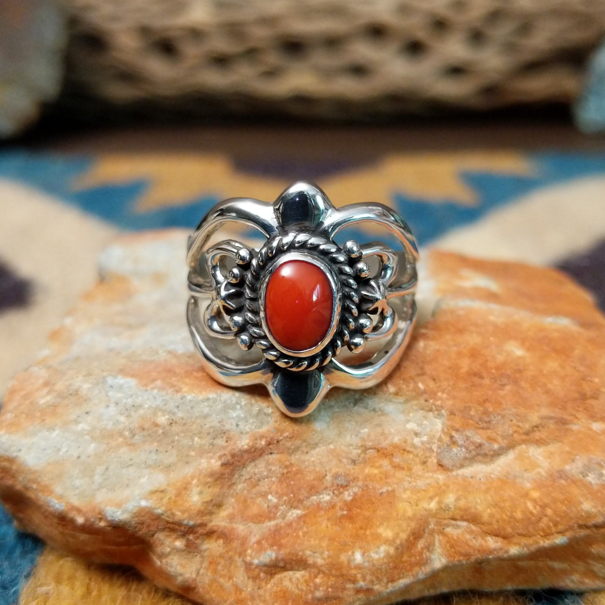 Handcrafted Navajo sterling silver ring by Raymond Coriz featuring an oval red coral cabochon surrounded by twisted rope, silver bead accents, and an ornate openwork floral design.