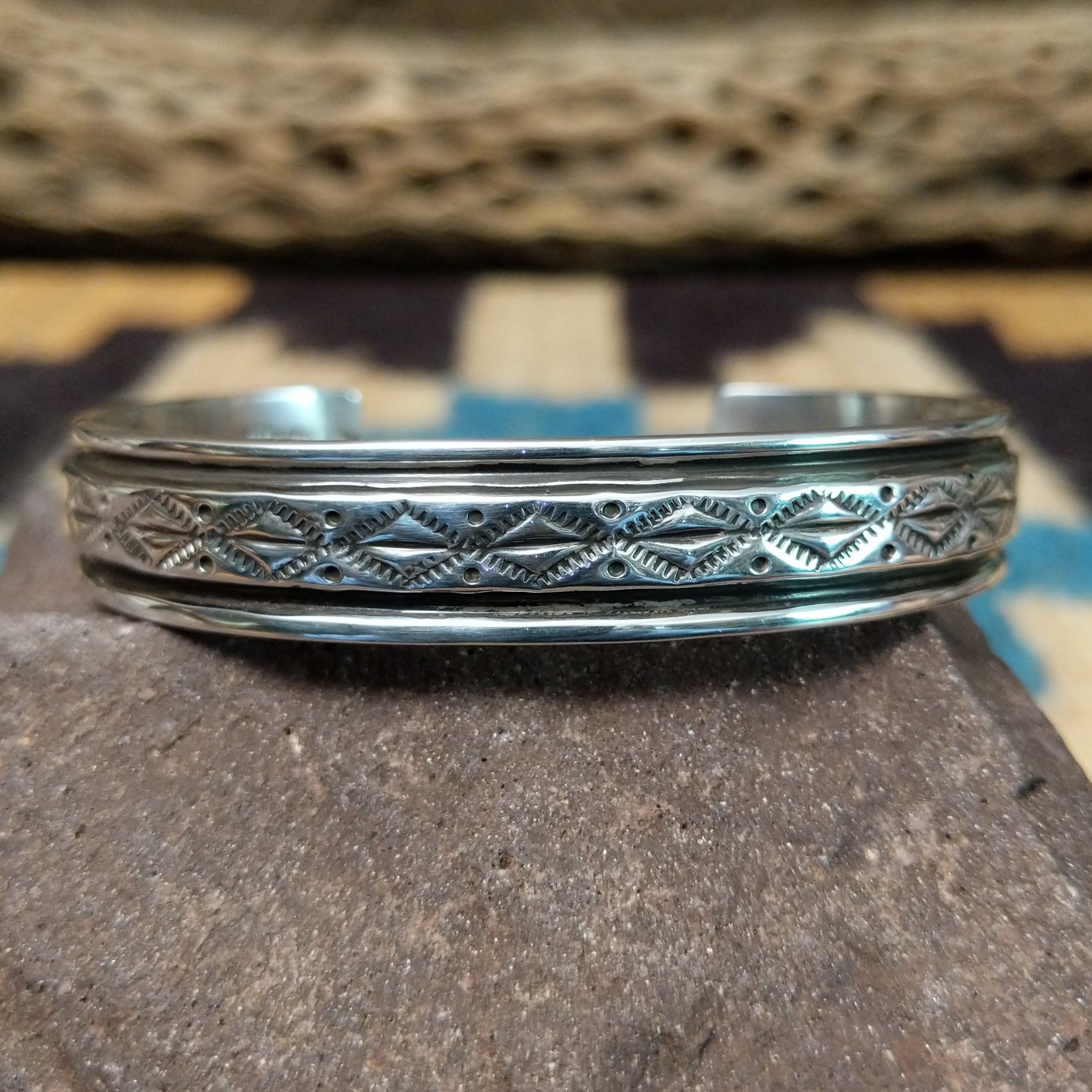 Ornate stamped sterling silver cuff by Diane Wylie, featuring intricate geometric hand-stamped patterns framed by polished silver borders in a handcrafted open cuff design.