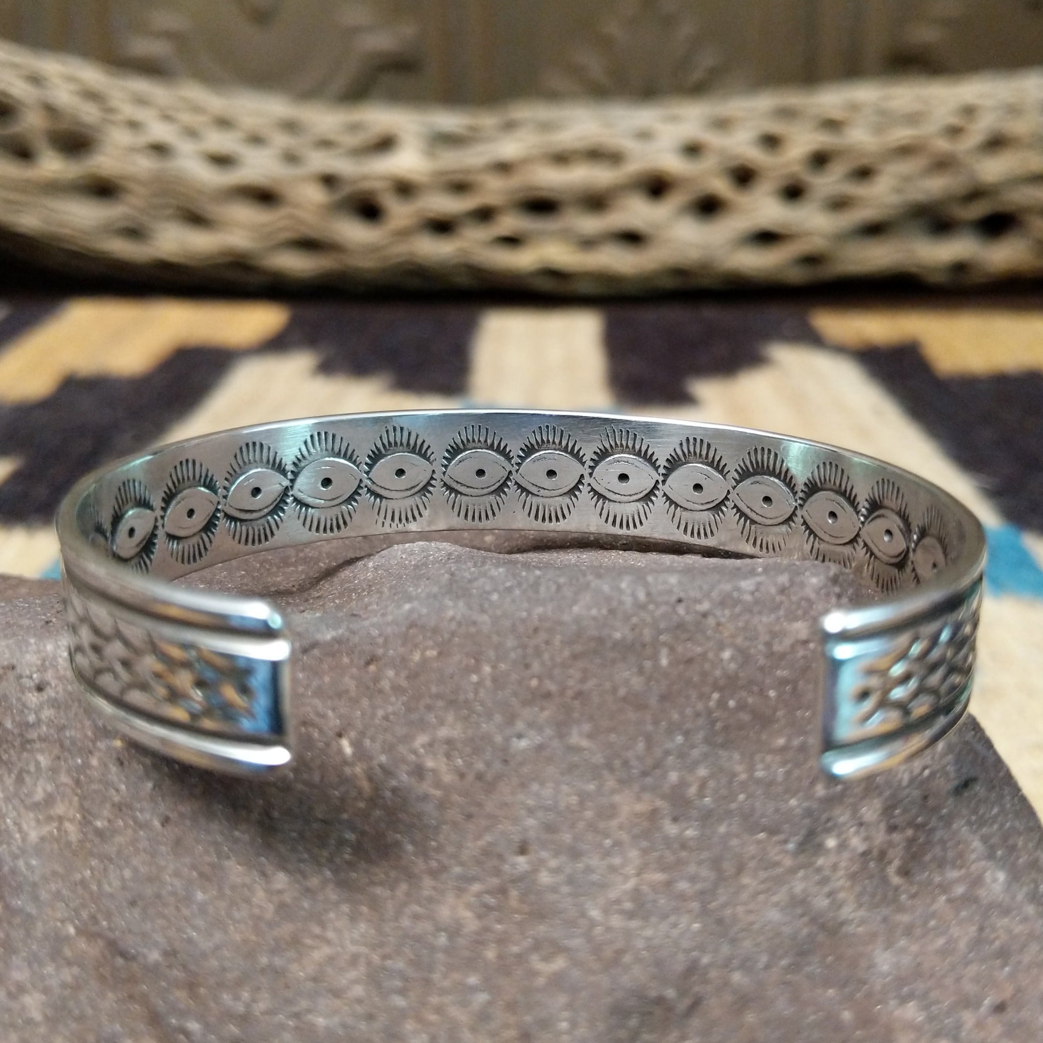 Ornate stamped sterling silver cuff by Diane Wylie, featuring intricate geometric hand-stamped patterns framed by polished silver borders in a handcrafted open cuff design. Underside details.