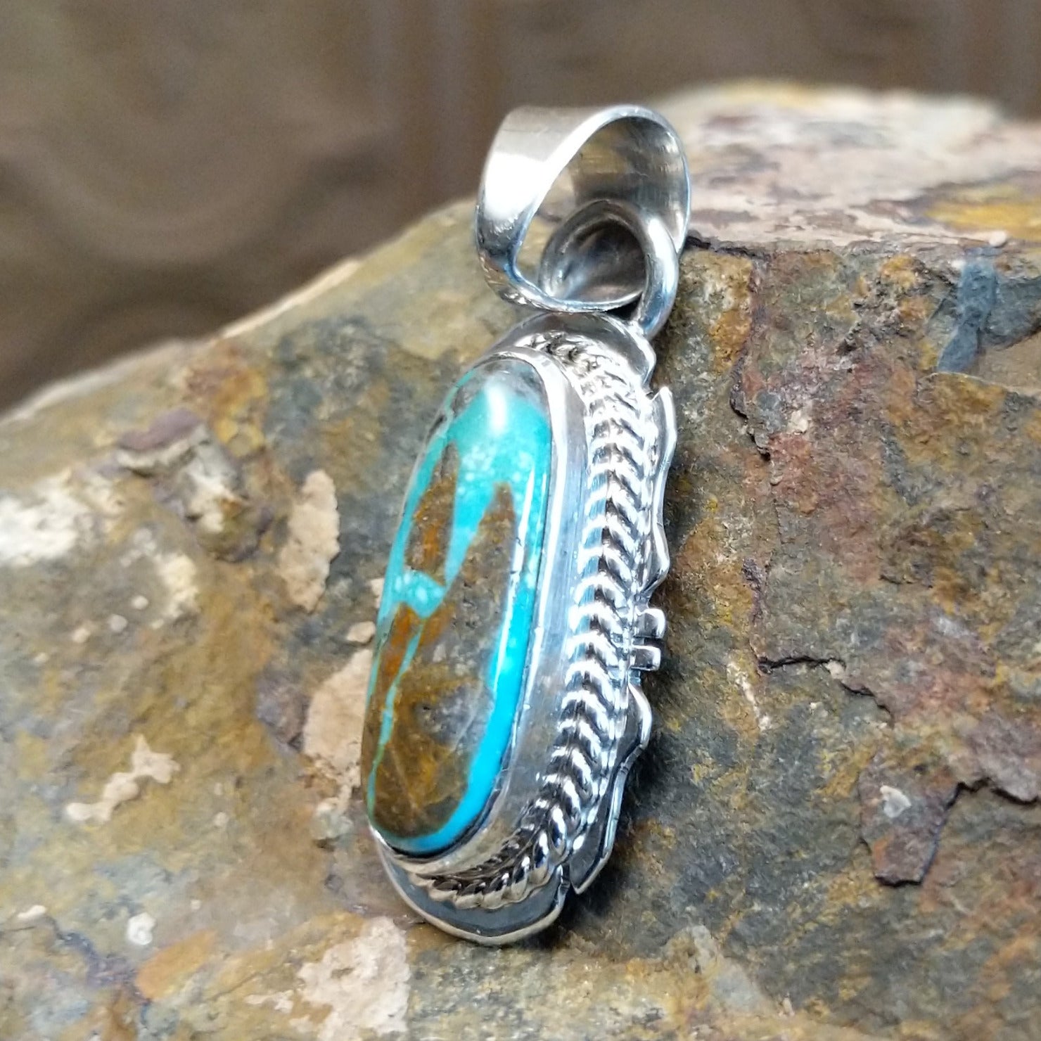 Handcrafted by Navajo artisan L.J., this capsule-shaped pendant features genuine #8 Turquoise set in sterling silver with a rope design accent.