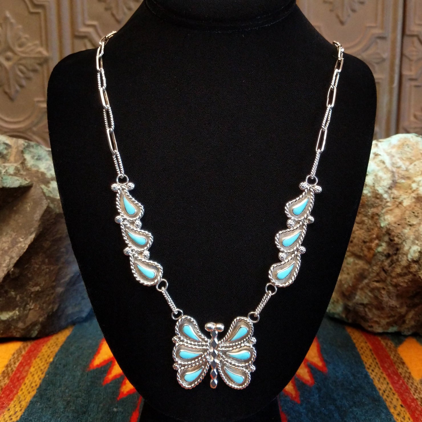 Butterfly-shaped necklace with turquoise stones on a black necklace bust.