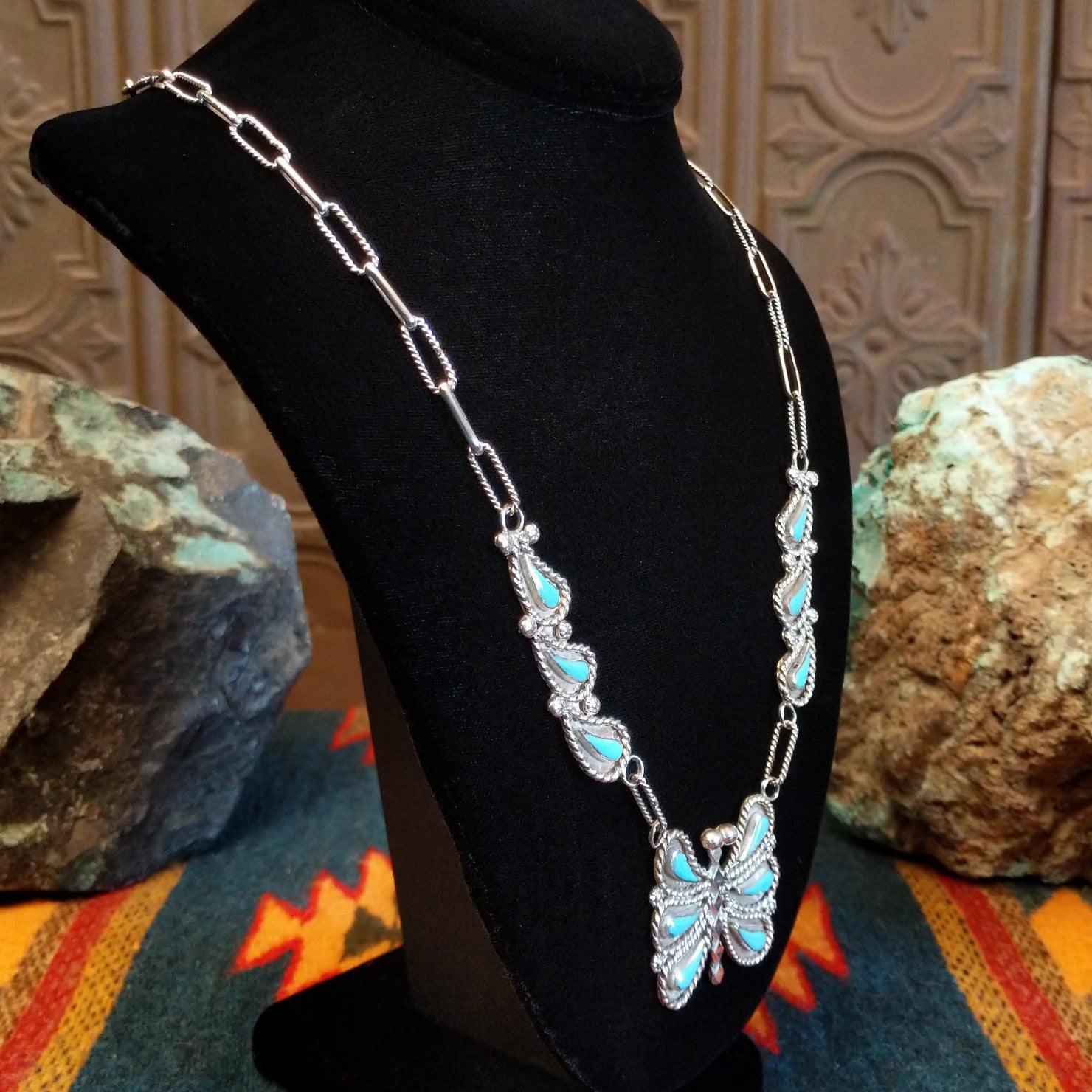 Butterfly necklace on a black stand, side view.