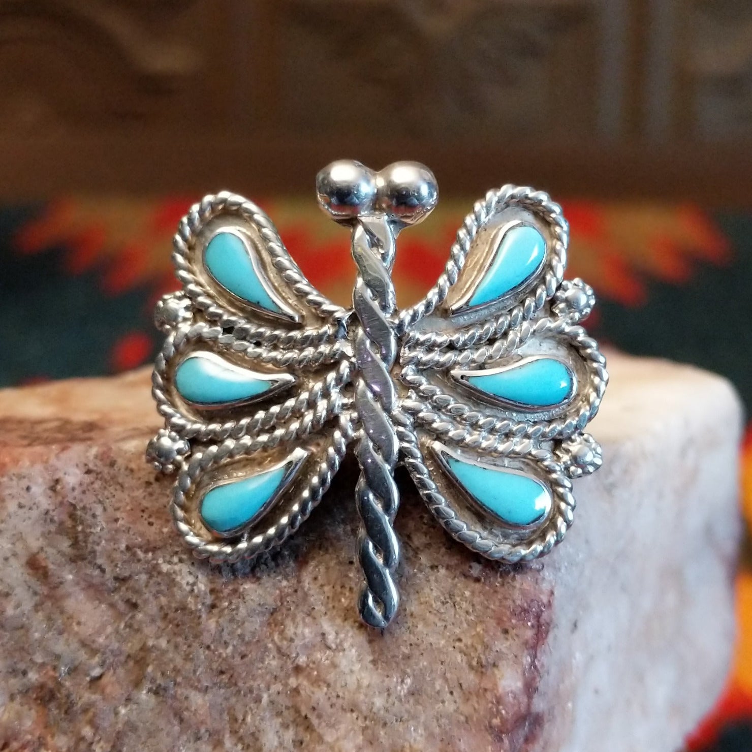 Butterfly-shaped silver and turquoise ring on a rock display.