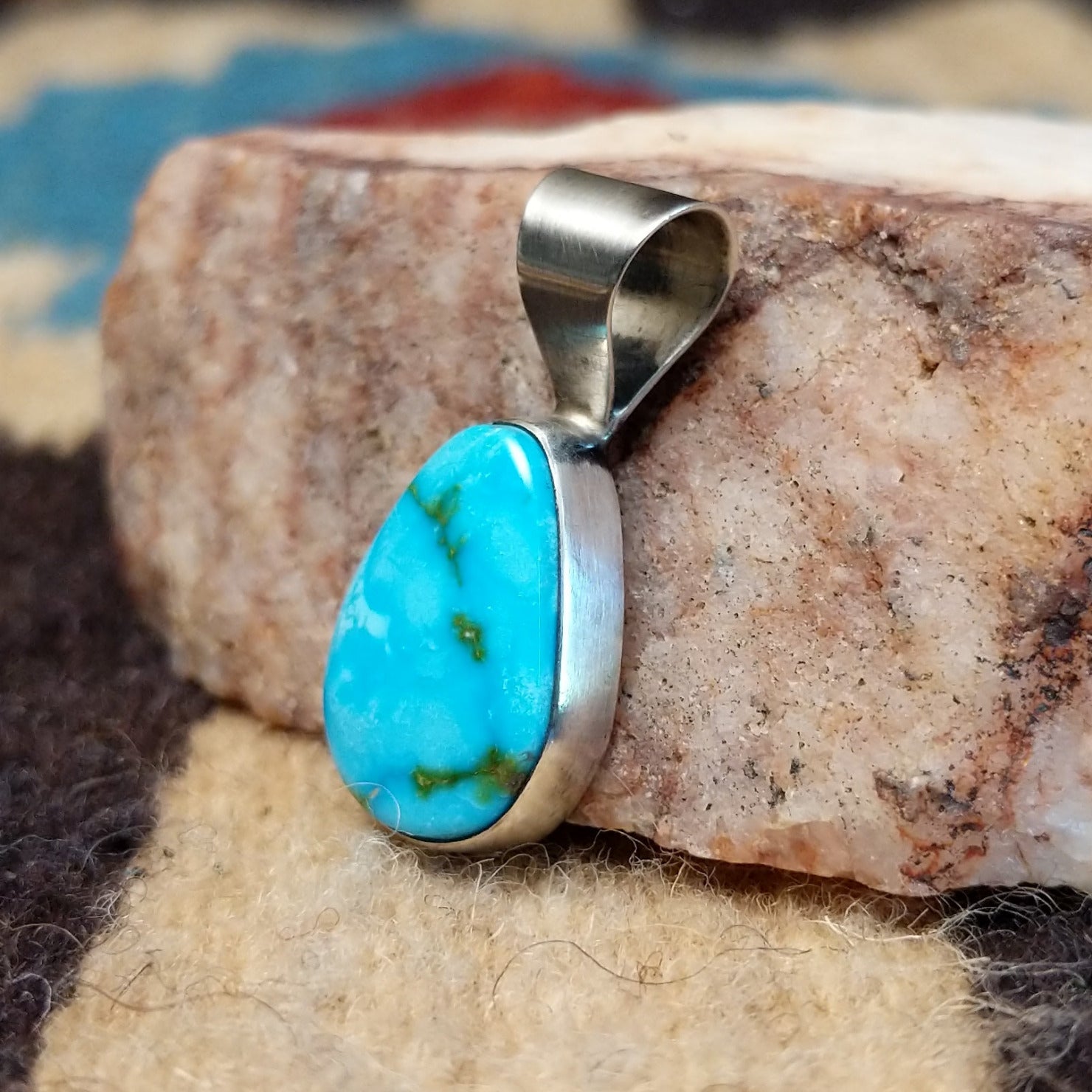 Ovoid sterling silver pendant featuring a polished Sonoran Gold turquoise stone with blue-green color and golden matrix, handcrafted by Native American artist Fred Guerro Jr. Side view.
