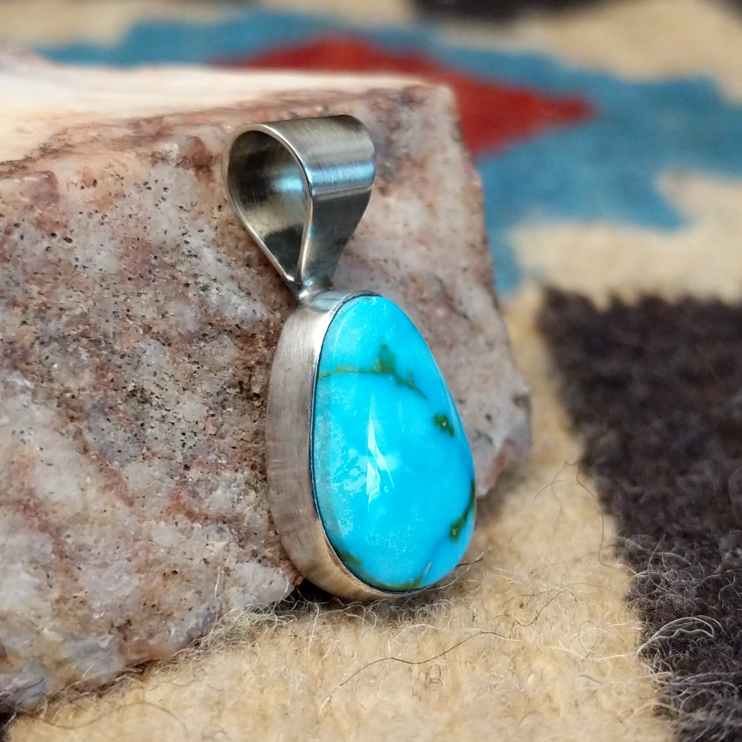 Ovoid sterling silver pendant featuring a polished Sonoran Gold turquoise stone with blue-green color and golden matrix, handcrafted by Native American artist Fred Guerro Jr. Side view.