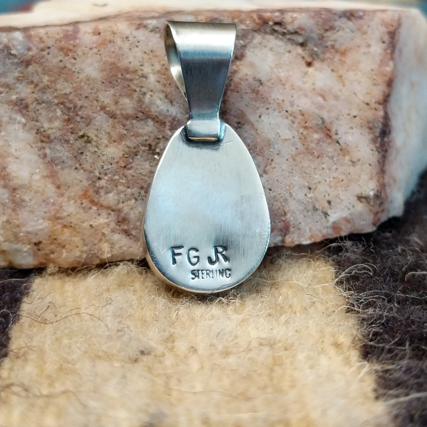 Ovoid sterling silver pendant featuring a polished Sonoran Gold turquoise stone with blue-green color and golden matrix, handcrafted by Native American artist Fred Guerro Jr. Back view with artisan and silver stamp.