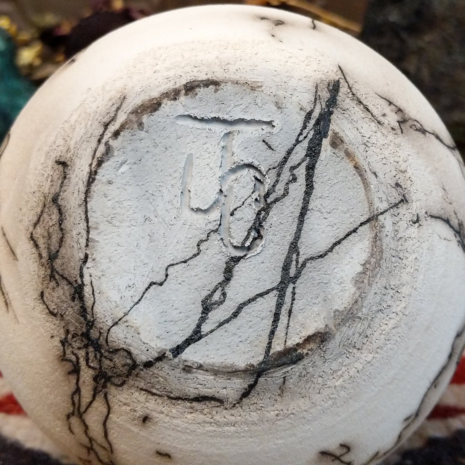 Small globe-shaped white horsehair pottery vase by local artisan Jim Calhoun featuring smoky organic markings, polished finish, and handcrafted Southwestern design. Underside view with artisan initials.