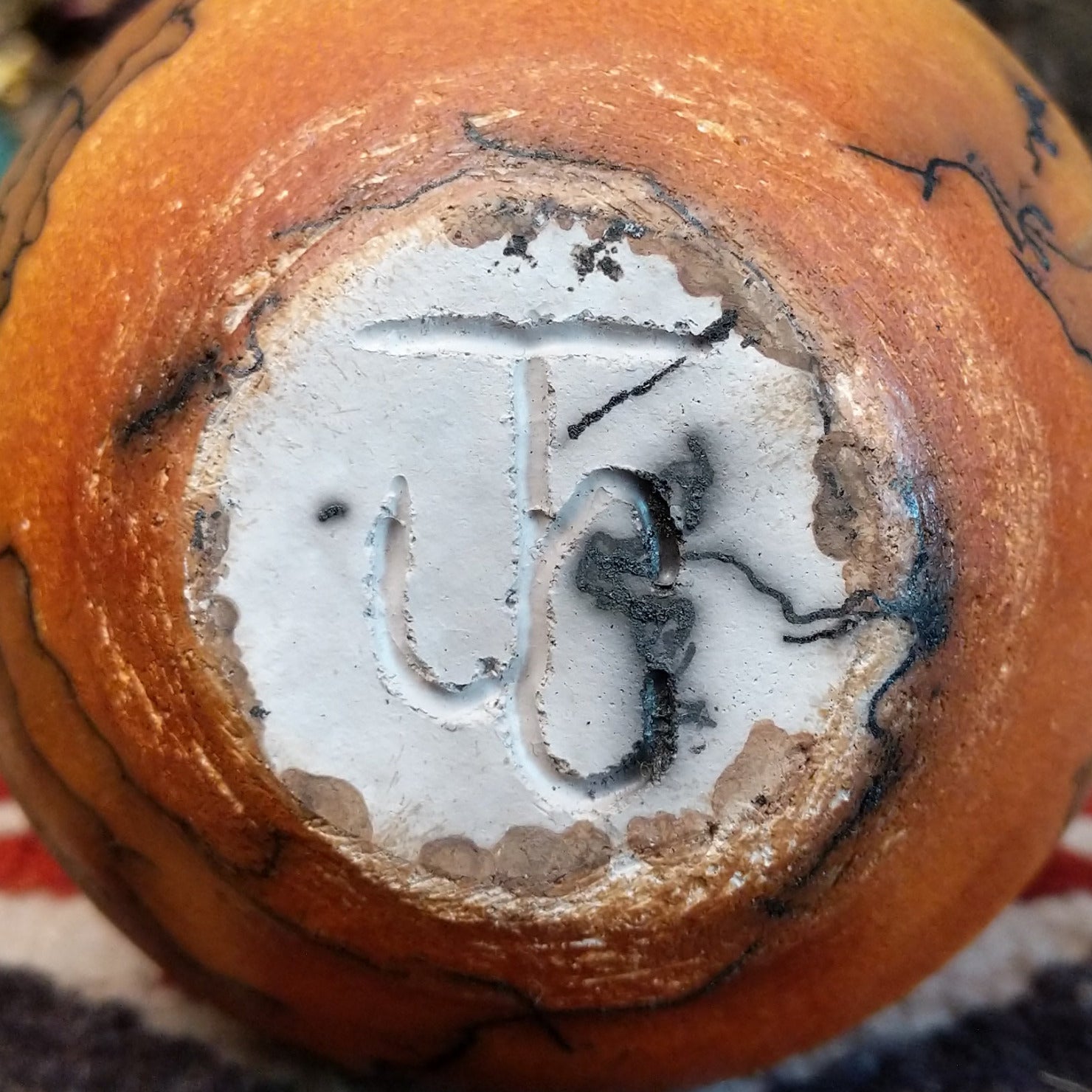 Small handcrafted terracotta horsehair vase with a rounded body and flared rim, decorated with black abstract horsehair firing patterns by artisan Jim Calhoun. Underside view with artisan initials.