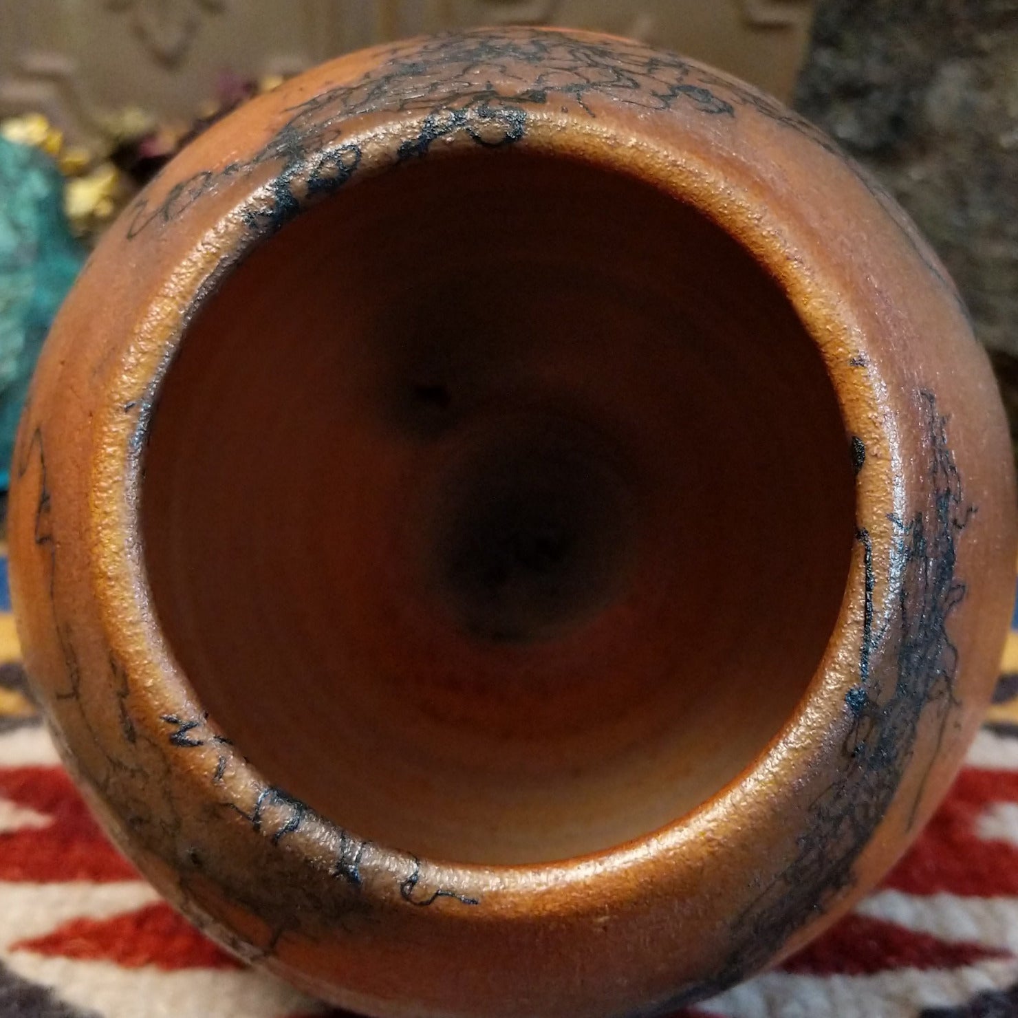 Small oval terracotta horsehair vase handcrafted by local artisan Jim Calhoun, featuring warm earthy clay tones and delicate black horsehair fire patterns on a smooth rounded surface. Top view.
