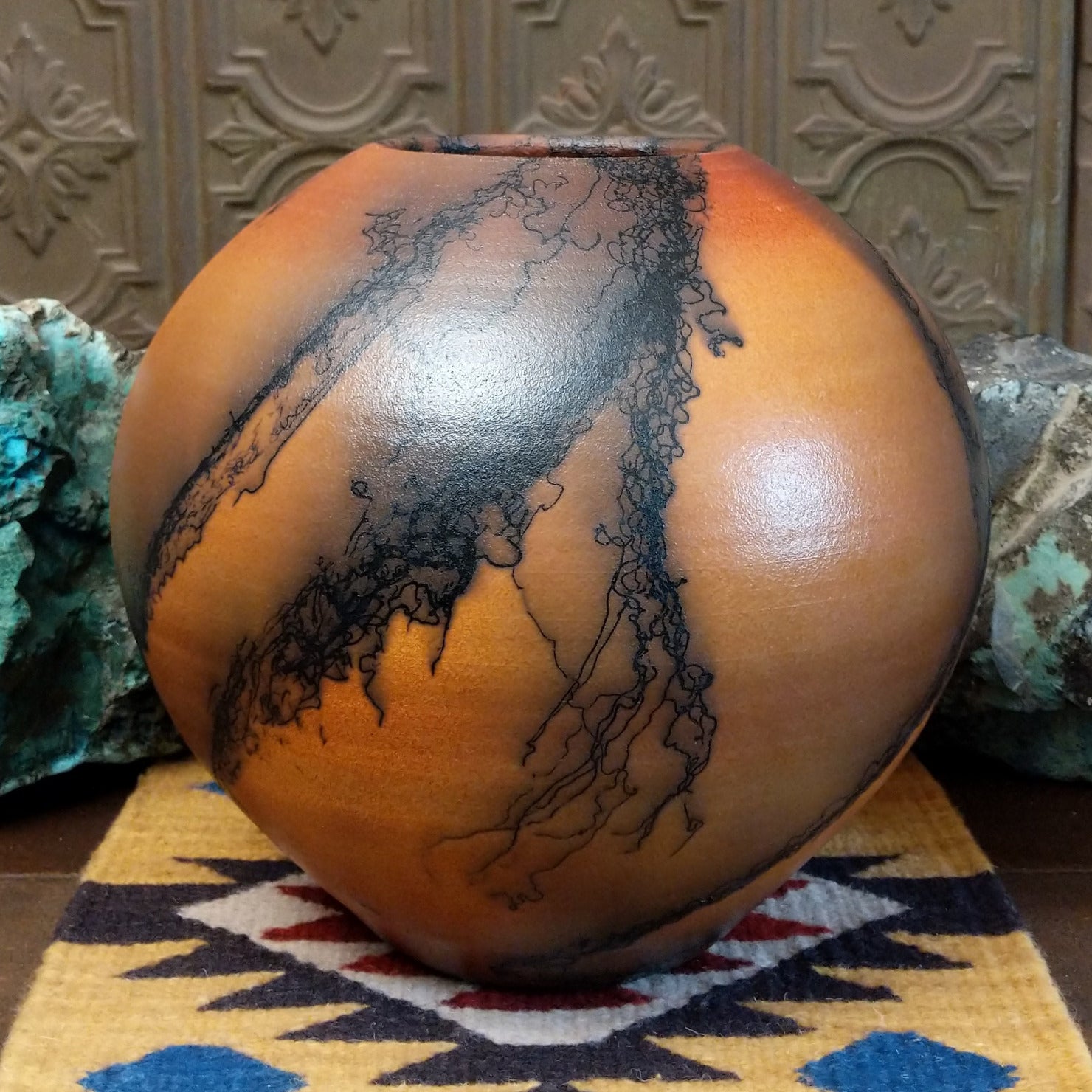 Large round terracotta horsehair pottery vessel handcrafted by local artisan Jim Calhoun, featuring warm clay tones and distinctive black horsehair fire patterns on a rounded surface.
