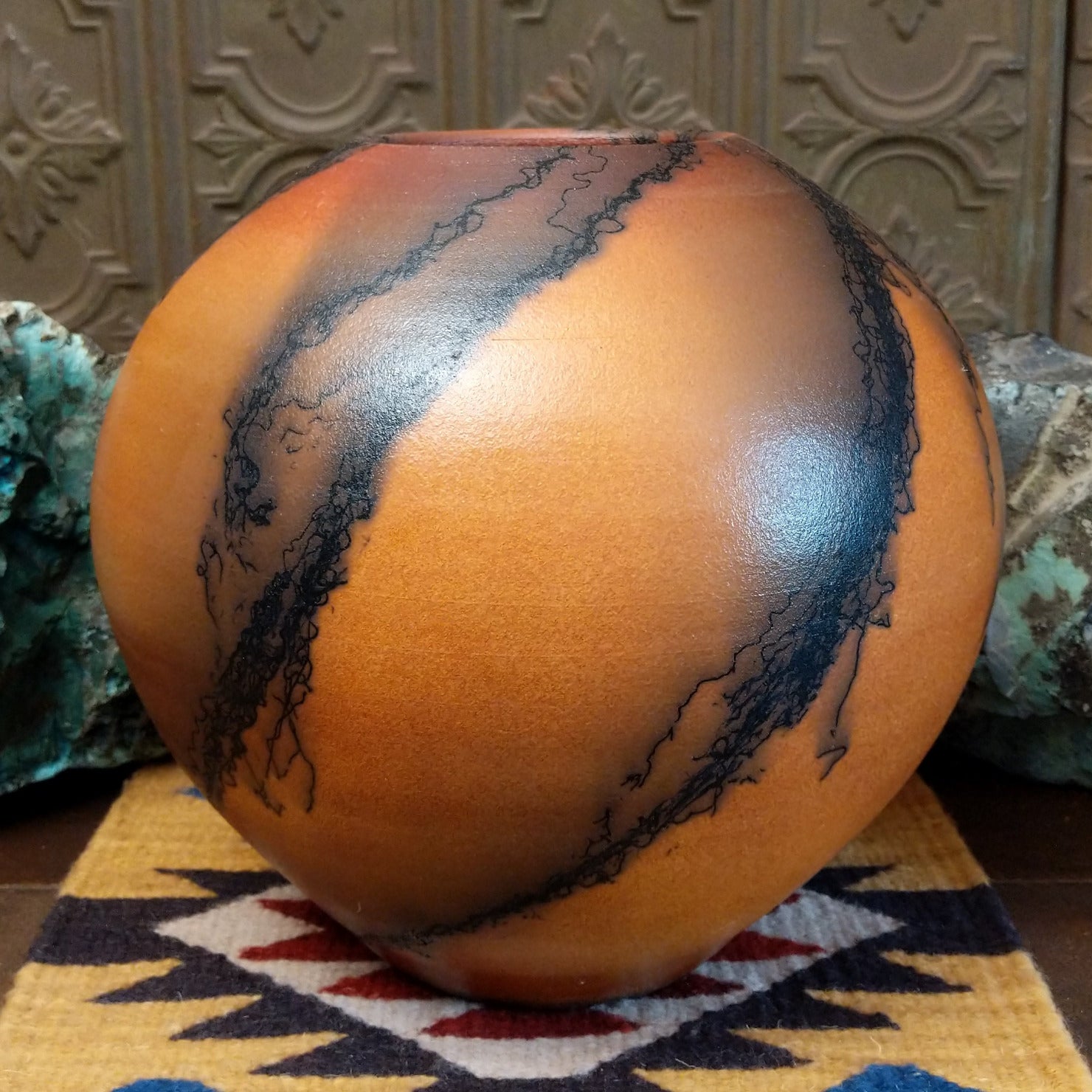 Large round terracotta horsehair pottery vessel handcrafted by local artisan Jim Calhoun, featuring warm clay tones and distinctive black horsehair fire patterns on a rounded surface.