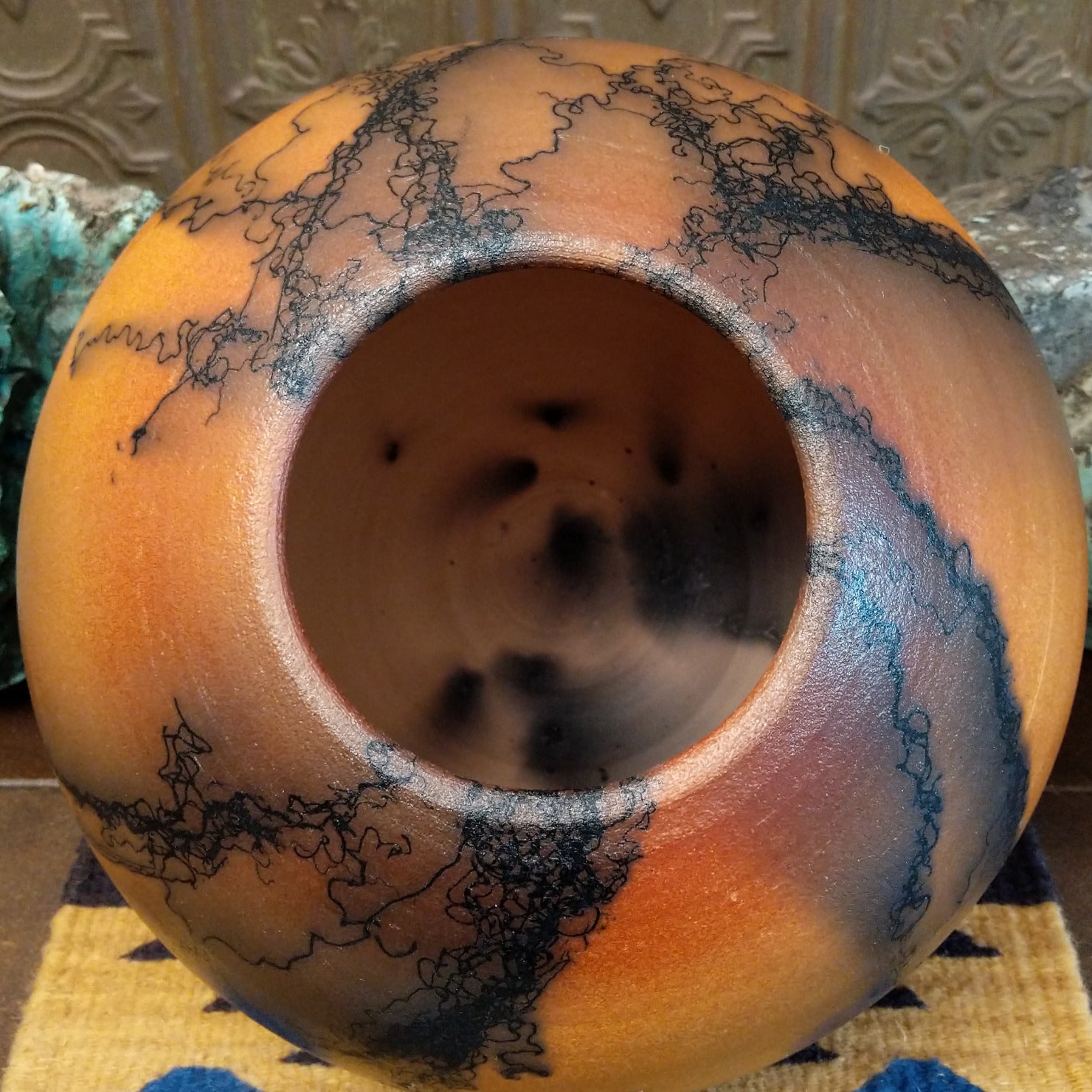 Large round terracotta horsehair pottery vessel handcrafted by local artisan Jim Calhoun, featuring warm clay tones and distinctive black horsehair fire patterns on a rounded surface. Top view.