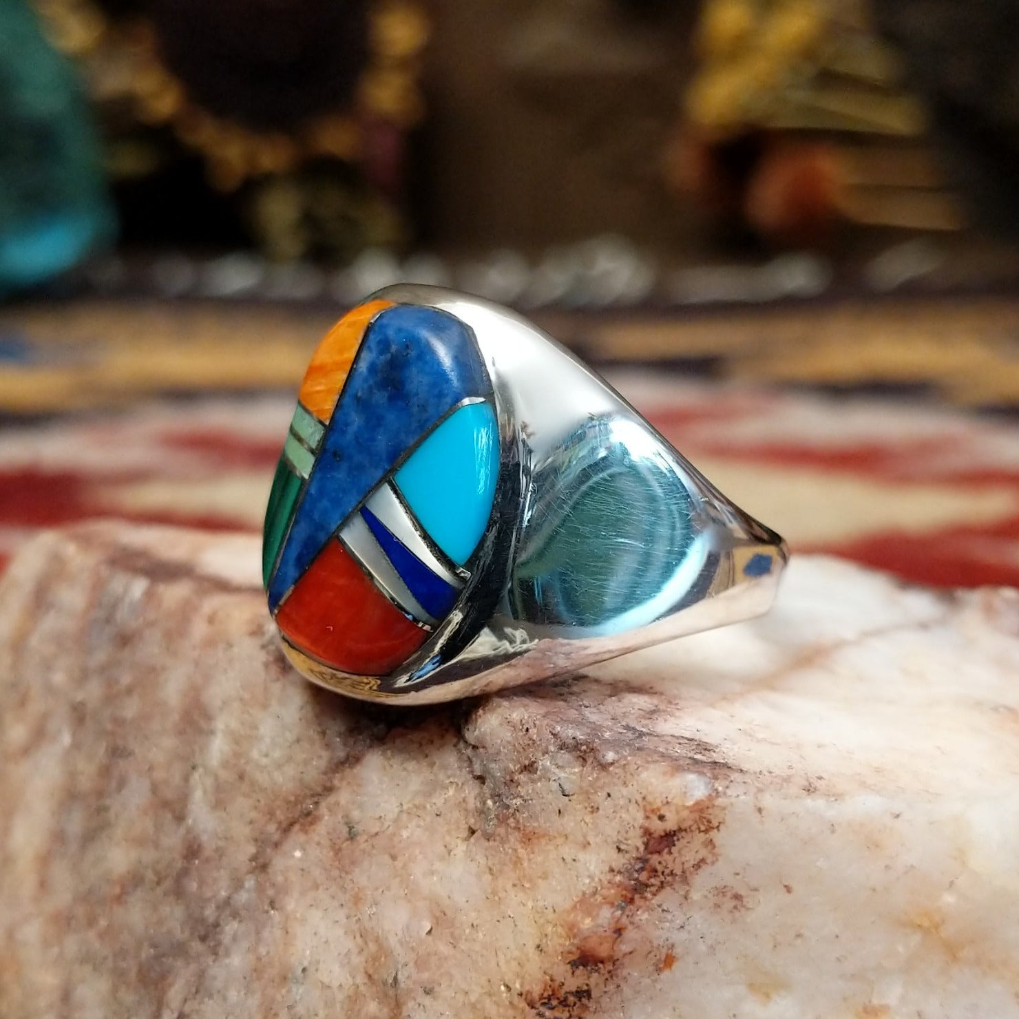 Handcrafted sterling silver multistone inlay ring by Navajo artist Bernadine Joe featuring Denim Lapis, Lapis, red and orange Spiny Oyster Shell, Mother of Pearl, Turquoise, and Malachite arranged in a colorful geometric mosaic design. Side view.