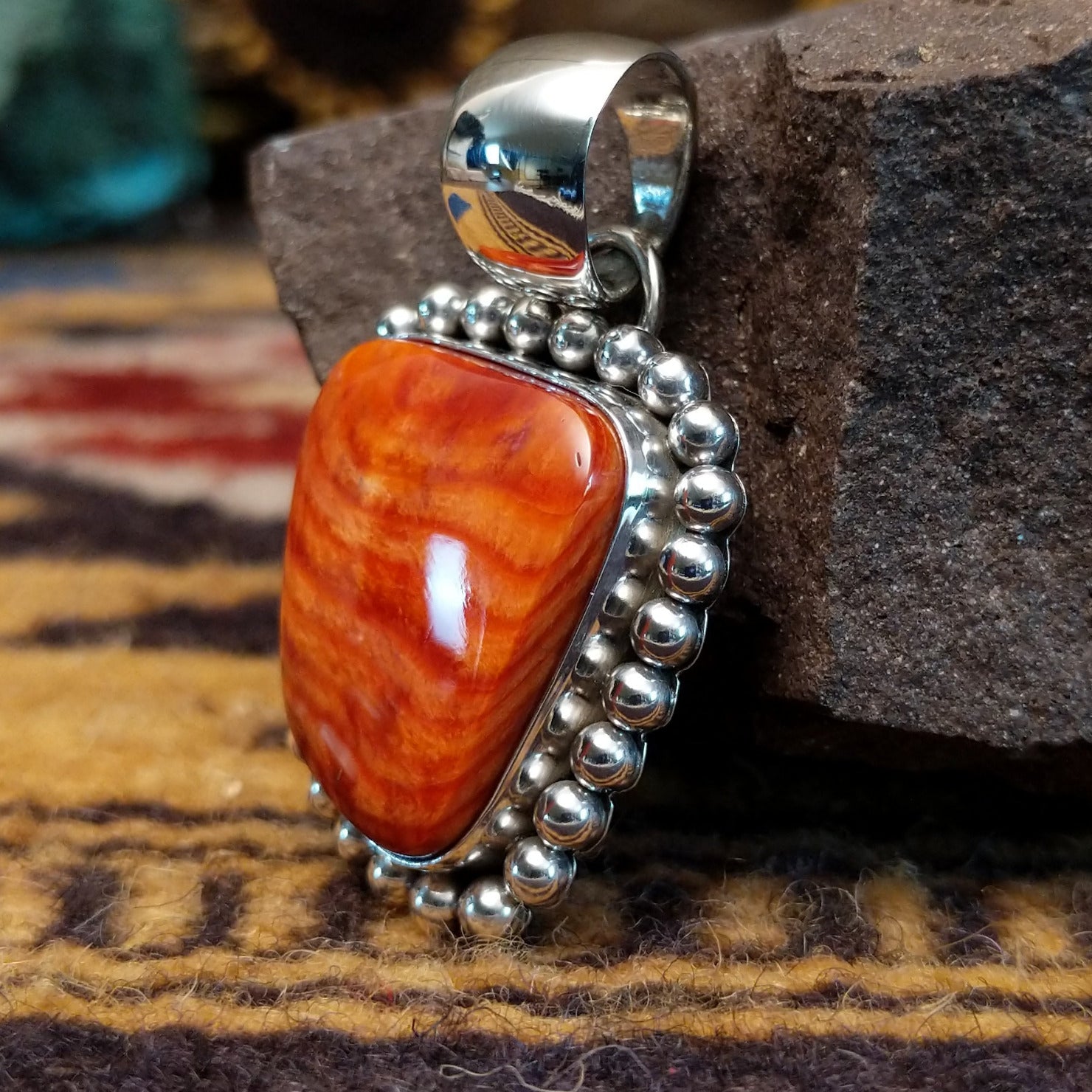 Handcrafted sterling silver pendant by Artie Yellowhorse featuring a red spiny oyster shell with dotted silver detailing in a Southwestern Native American design. Side view.