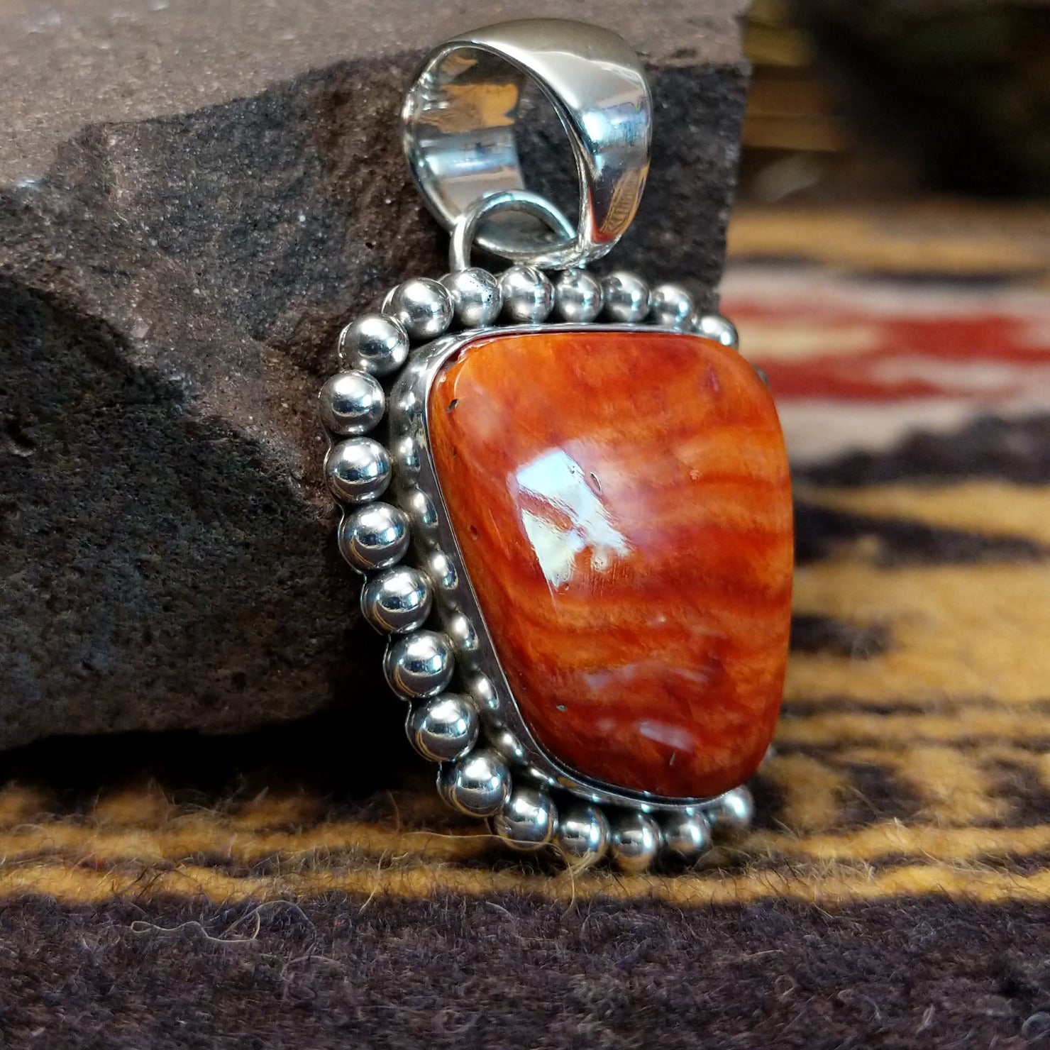 Handcrafted sterling silver pendant by Artie Yellowhorse featuring a red spiny oyster shell with dotted silver detailing in a Southwestern Native American design. Side view.
