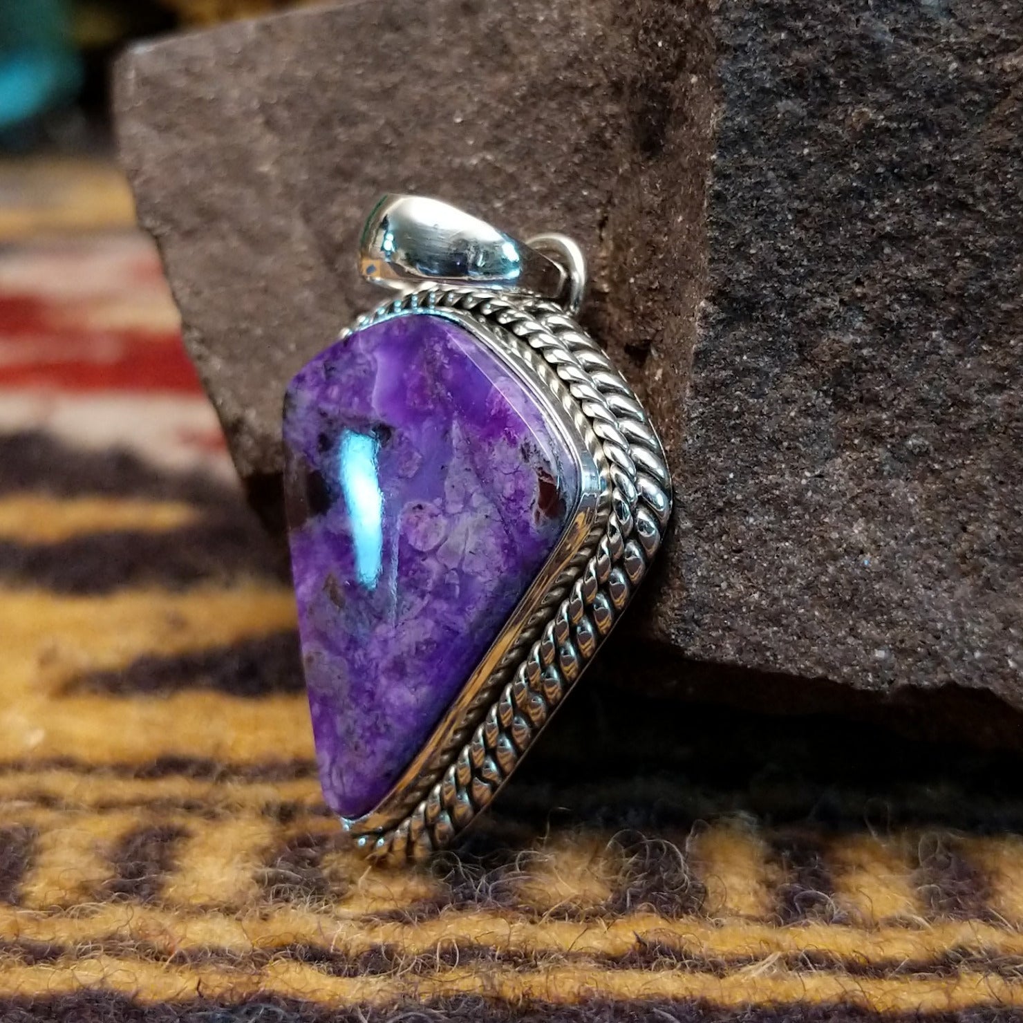 Handcrafted sterling silver pendant by Artie Yellowhorse featuring a deep purple sugilite stone in a polished Southwestern Native American design. Side view.
