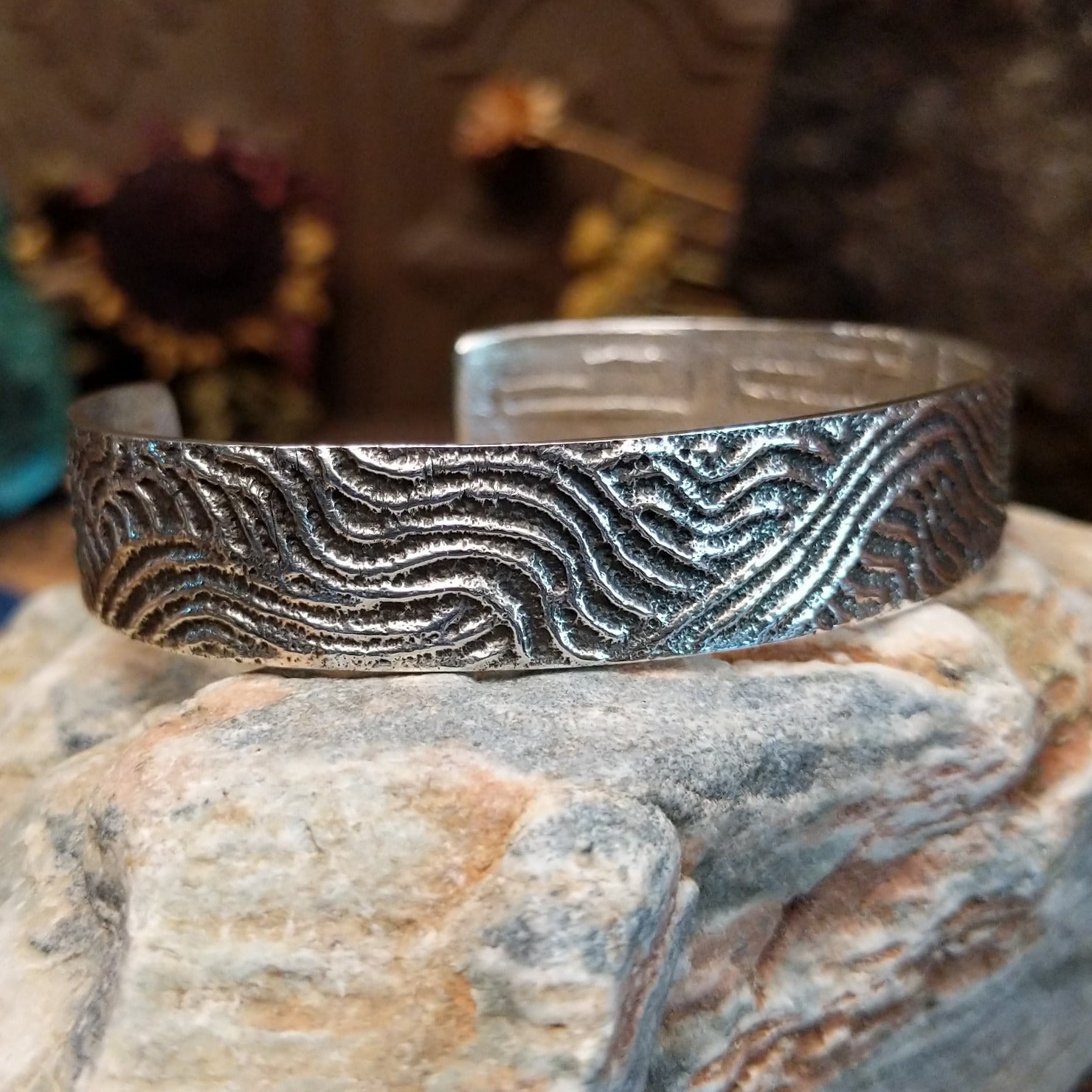 Handcrafted sterling silver cuff bracelet by Dino Garcia featuring a wavy tufa cast design with textured organic detailing in a Southwestern Native American style. Side view.