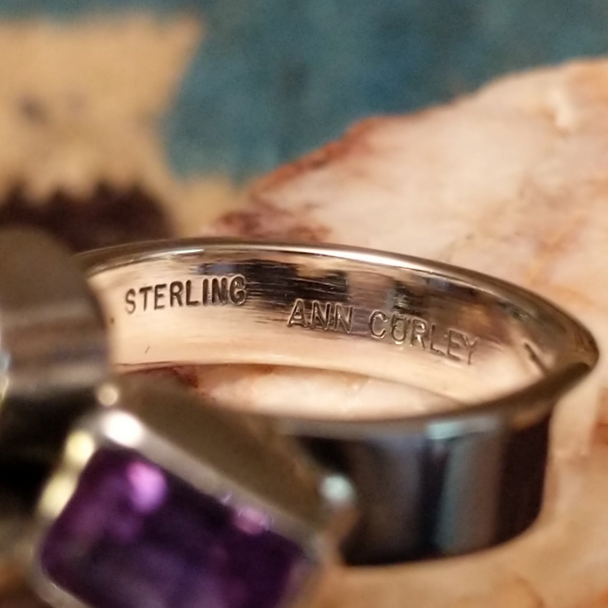 Amethyst ring by Ann Curley, featuring four faceted purple amethyst gemstones in round, square, rectangular, and pear shapes set in a handcrafted sterling silver ring. Artisan and Sterling Silver stamp.