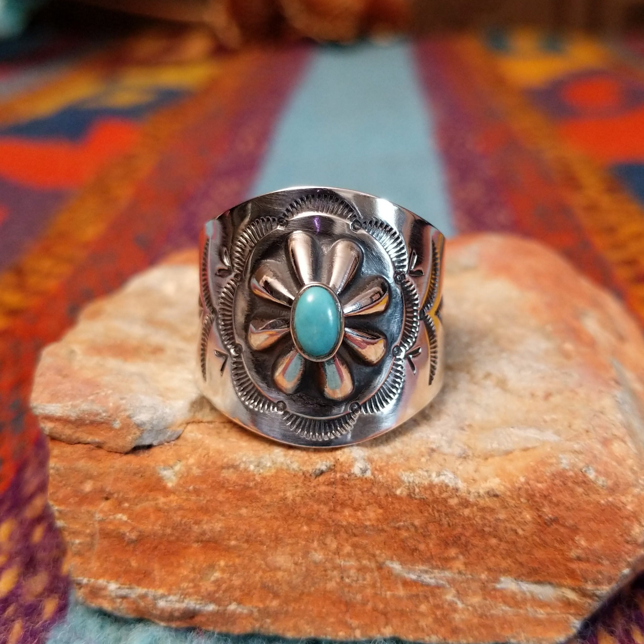 Raised #8 Turquoise Ring by Chris Billie featuring an oval turquoise stone centered within a raised silver flower, surrounded by detailed stamped and oxidized silverwork on a wide band.