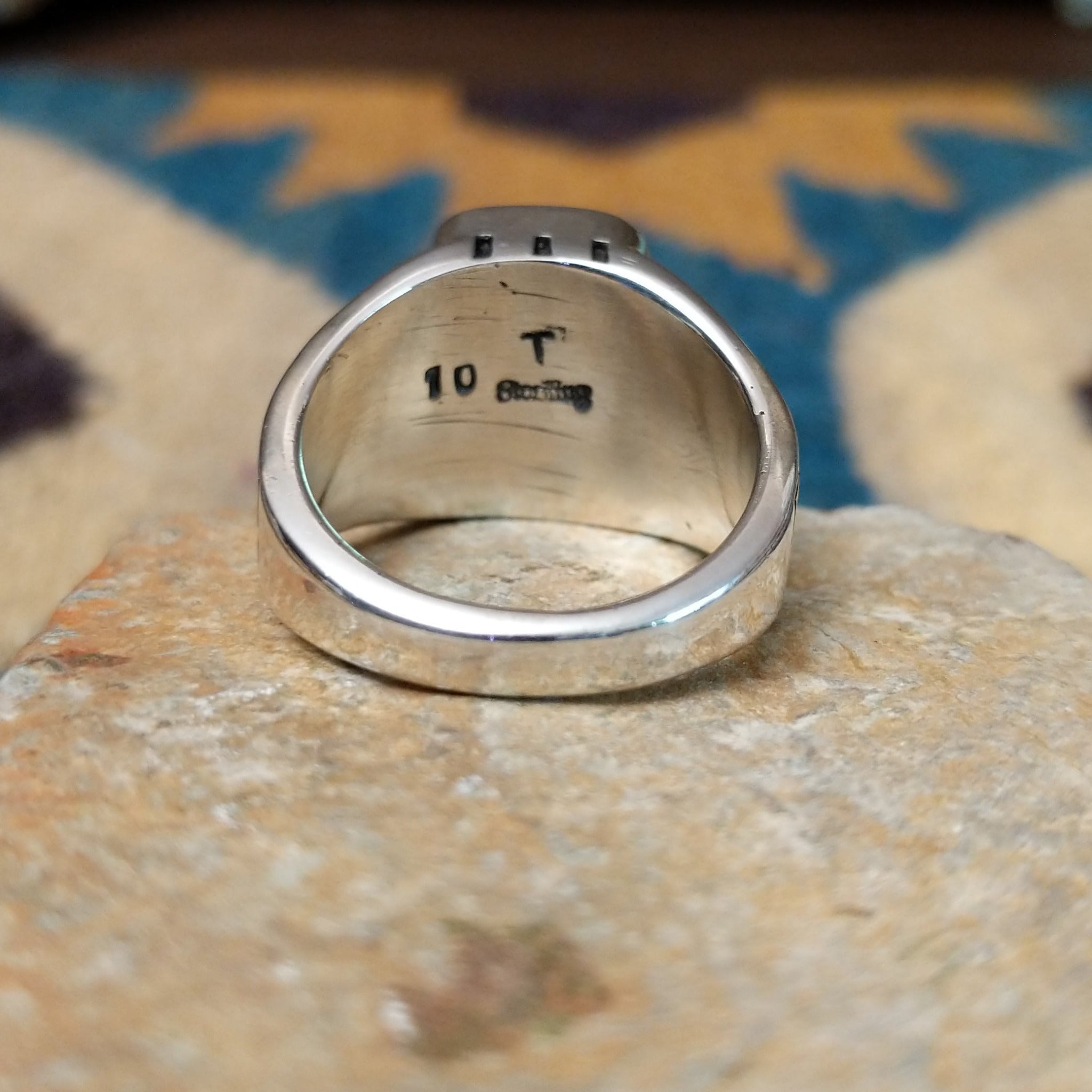 Handcrafted Navajo sterling silver ring by Terry Wood featuring a raised rectangular charoite cabochon with natural purple swirling patterns, set in a polished silver bezel with geometric detailing on the band; underside view.