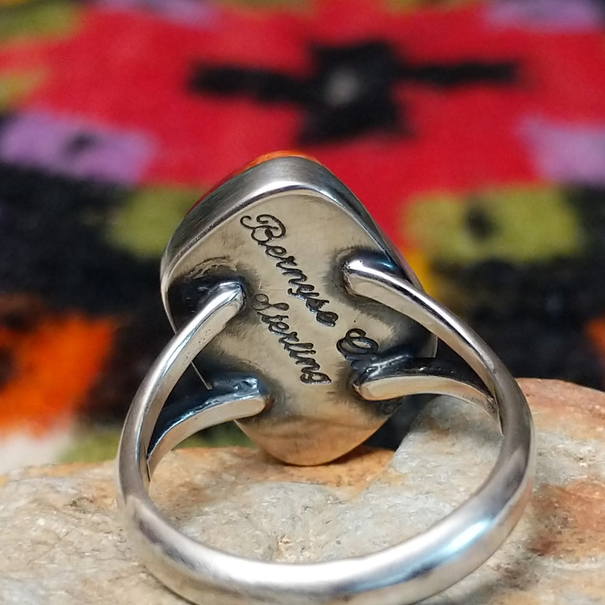 Red spiny oyster shell ring by Bernyse Chavez with an irregular polished stone and split silver band. Close up of the artist's stamped signature.