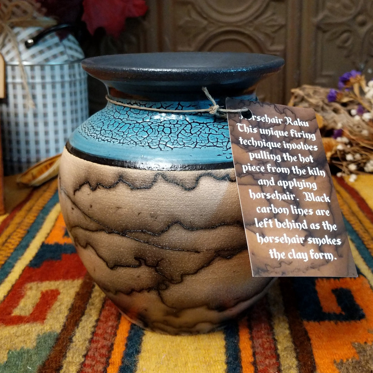 Round horsehair pottery vase by Roger Calhoun with a wide black rim, crackled turquoise-blue shoulder, and smoky black horsehair patterns across a cream-colored body.