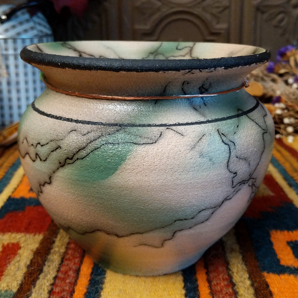 This elegant Round Mottled Green Horsehair Pottery by Roger Calhoun features a rounded ceramic vase with a wide black-rimmed opening, soft green accents, intricate black horsehair patterns, and a copper wire accented with a green bead.