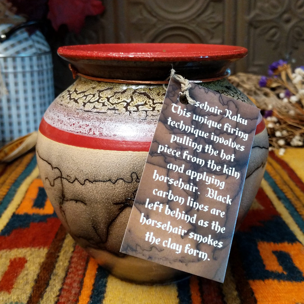 Round horsehair pottery vase by Roger Calhoun with a wide red rim, gold and lavender crackled shoulder, red accent band, and smoky black horsehair markings across a cream-colored body.