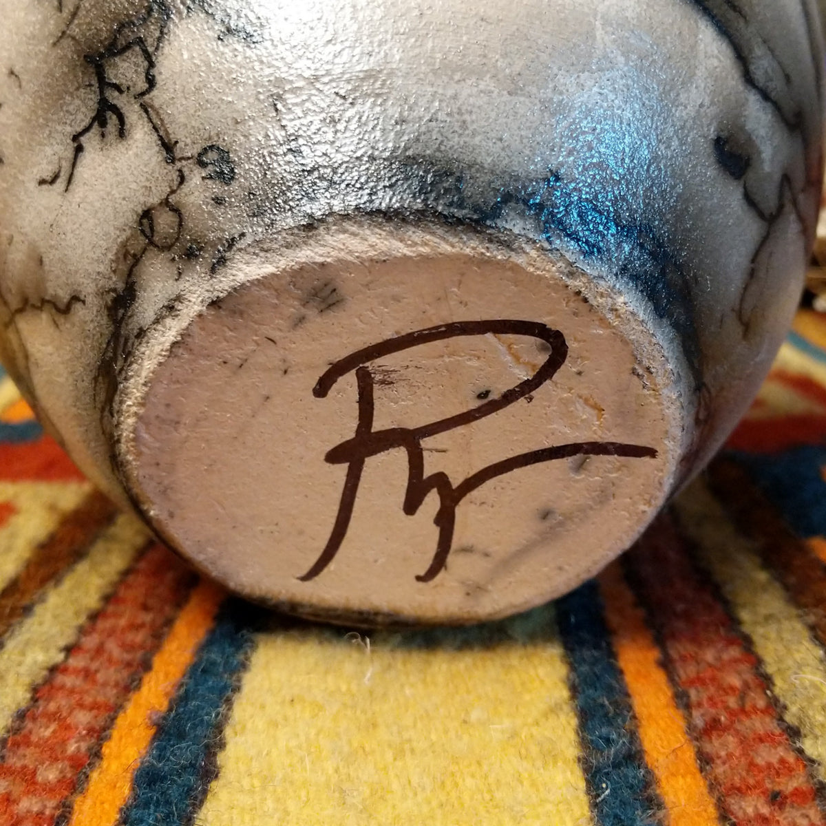 Close-up of the underside of Roger Calhoun's horsehair pottery, showing the artist's hand-painted initials on the unglazed base.