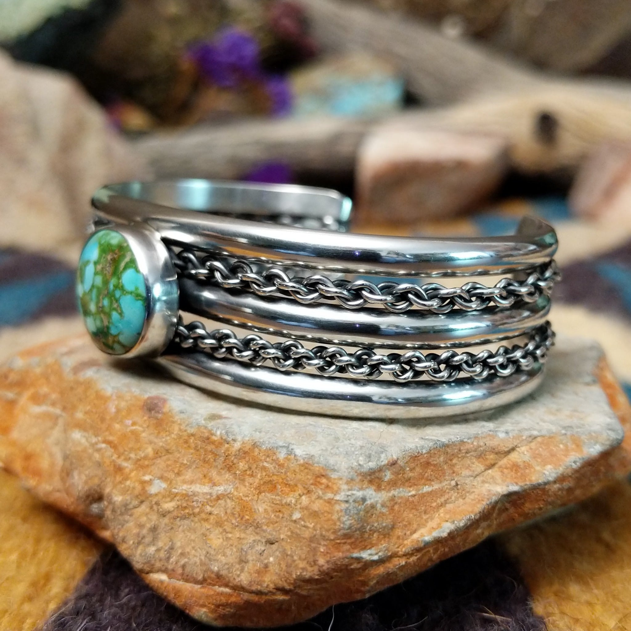 Handcrafted sterling silver cuff by H.R.M. featuring a round Sonoran Gold turquoise cabochon centered between polished silver bands with dual oxidized chain accents; side view.