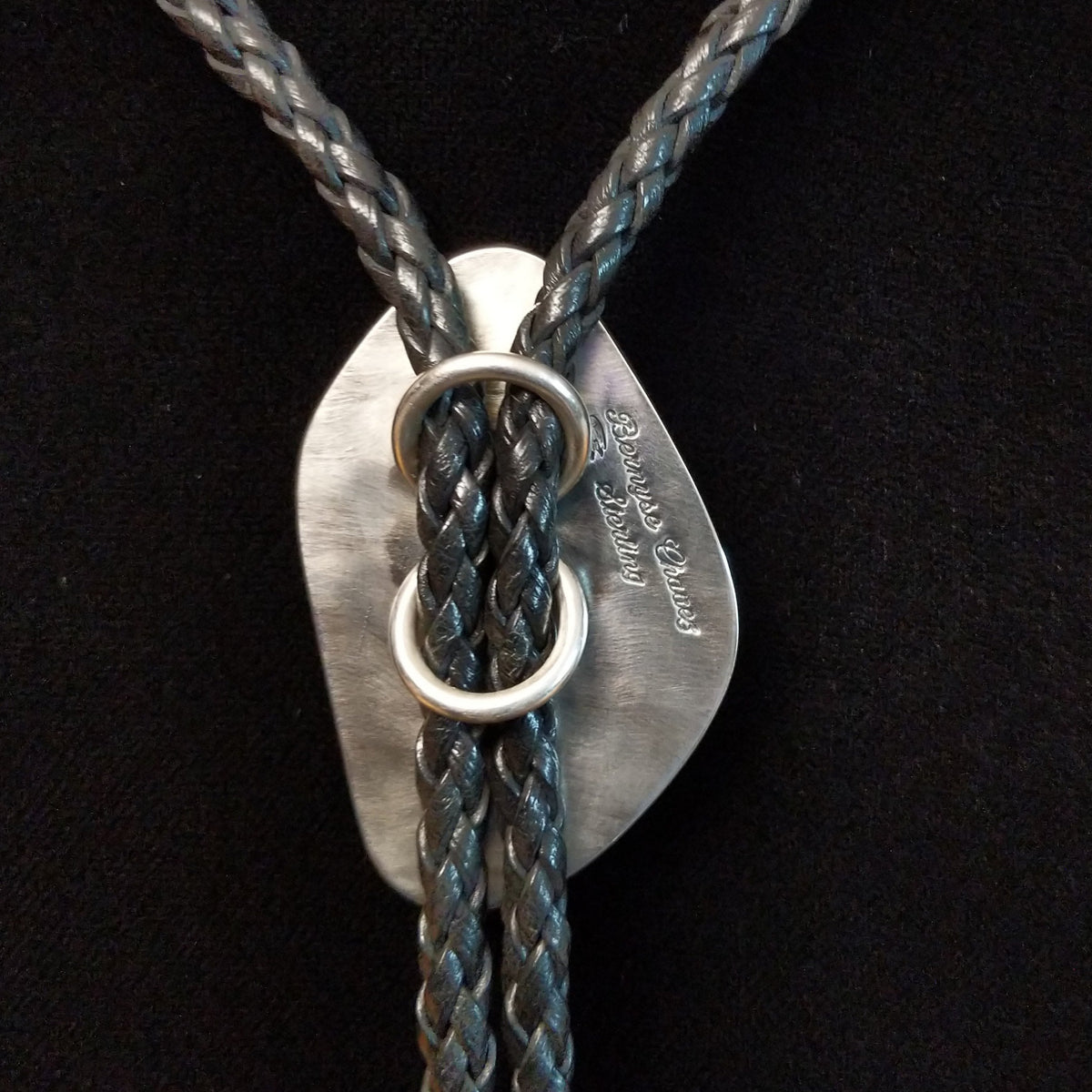 A braided leather bolo tie necklace, displayed on a black velvet mannequin bust. The tie features the artist and Sterling Silver stamp on back.
