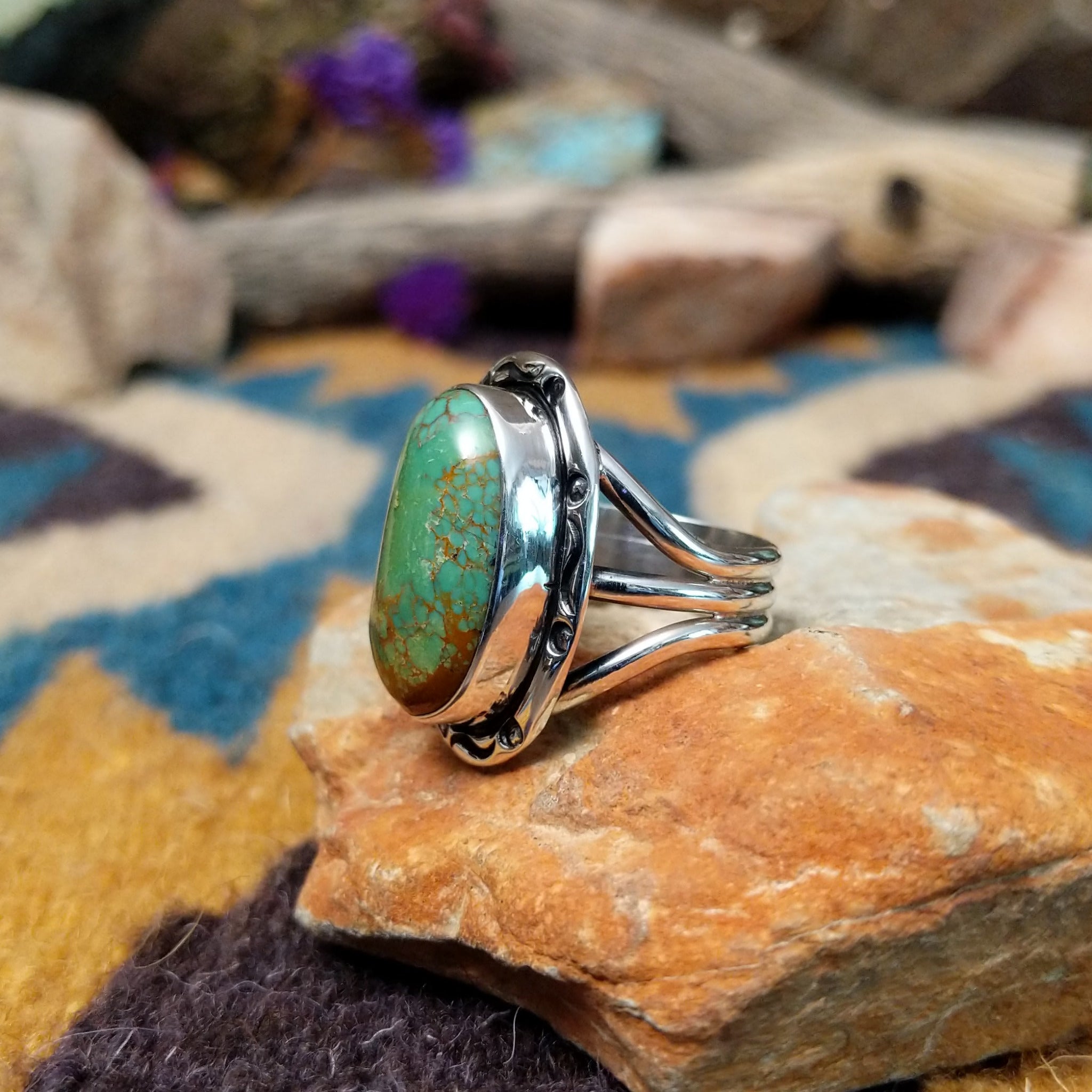 Handcrafted sterling silver ring featuring an elongated oval Royston turquoise cabochon with vivid green tones and golden-brown matrix, set in an ornate oxidized silver bezel with decorative bead accents; side view.