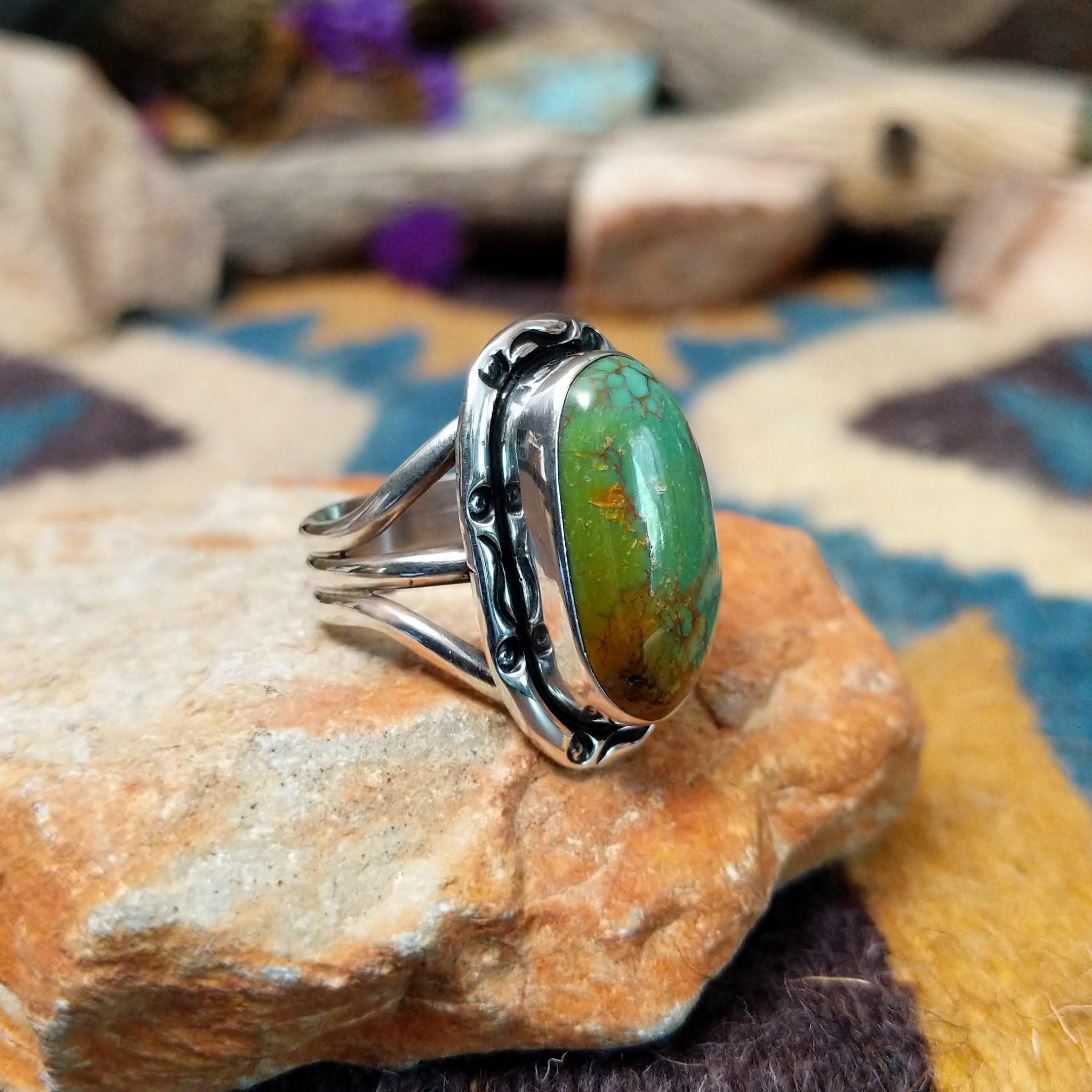 Handcrafted sterling silver ring featuring an elongated oval Royston turquoise cabochon with vivid green tones and golden-brown matrix, set in an ornate oxidized silver bezel with decorative bead accents; side view.