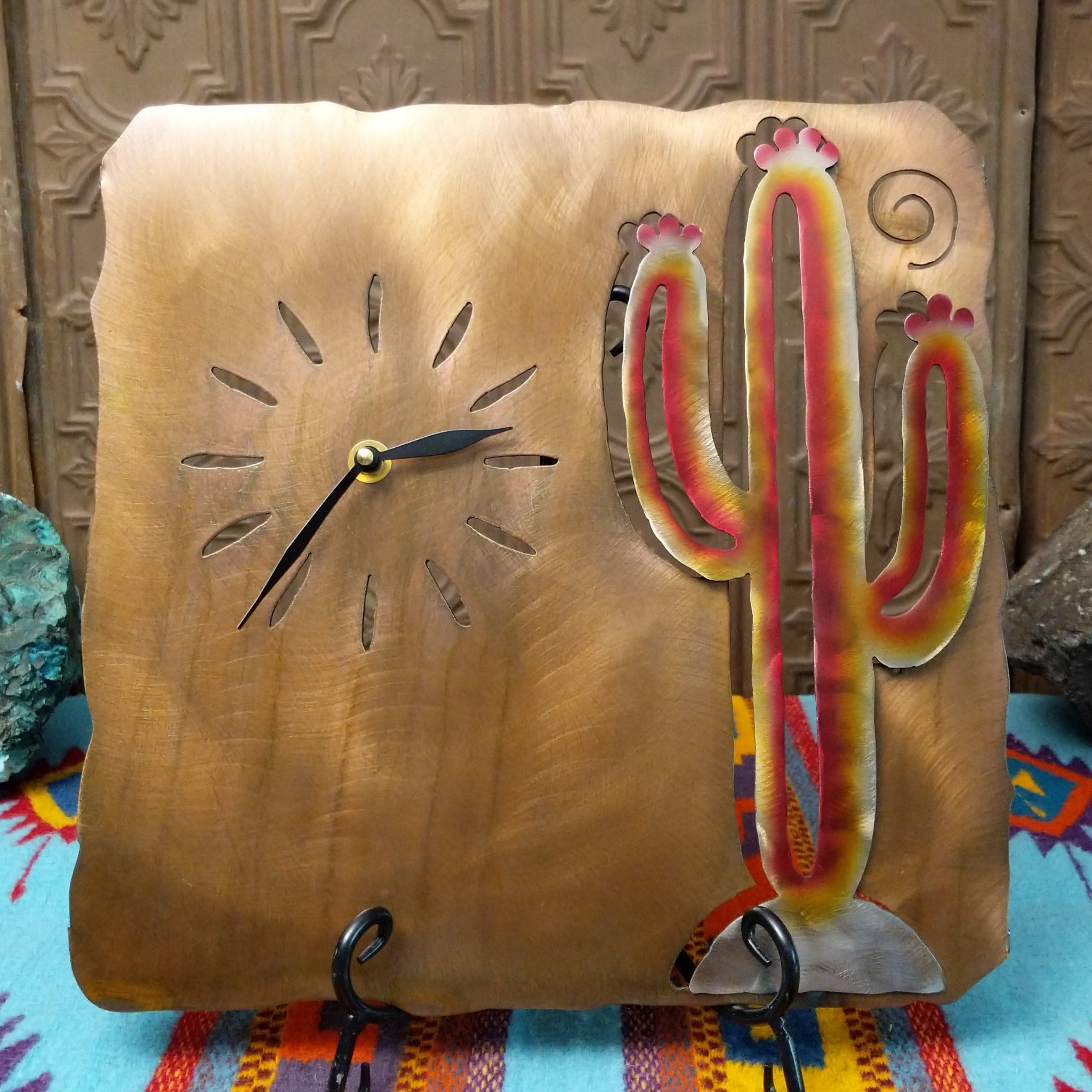 Handcrafted Crooks Design metal clock featuring a colorful red, yellow, and cream saguaro cactus on a brushed warm-gold background with cutout hour markers and black clock hands.