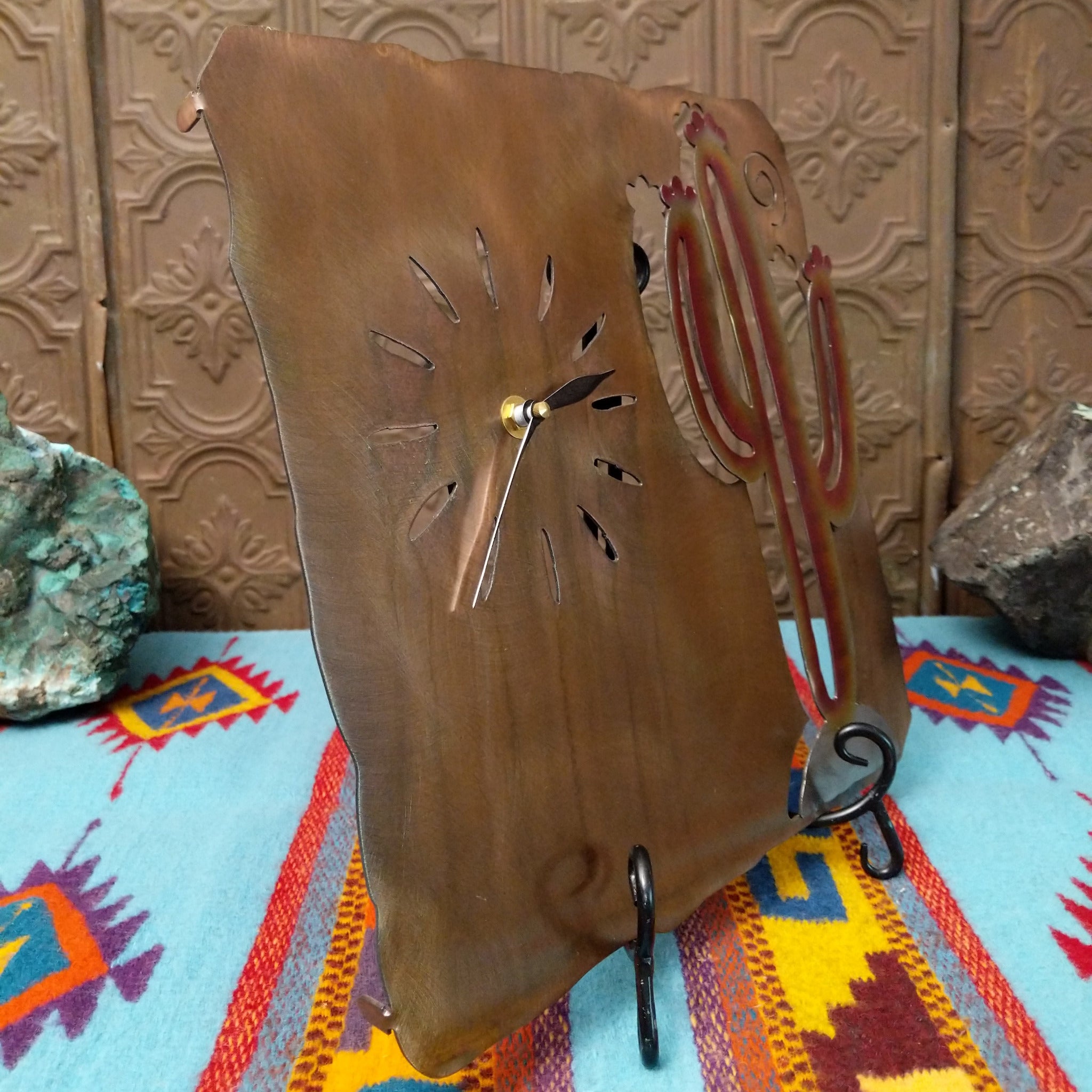 Handcrafted Crooks Design metal clock featuring a colorful red, yellow, and cream saguaro cactus on a brushed warm-gold background with cutout hour markers and black clock hands; side view.